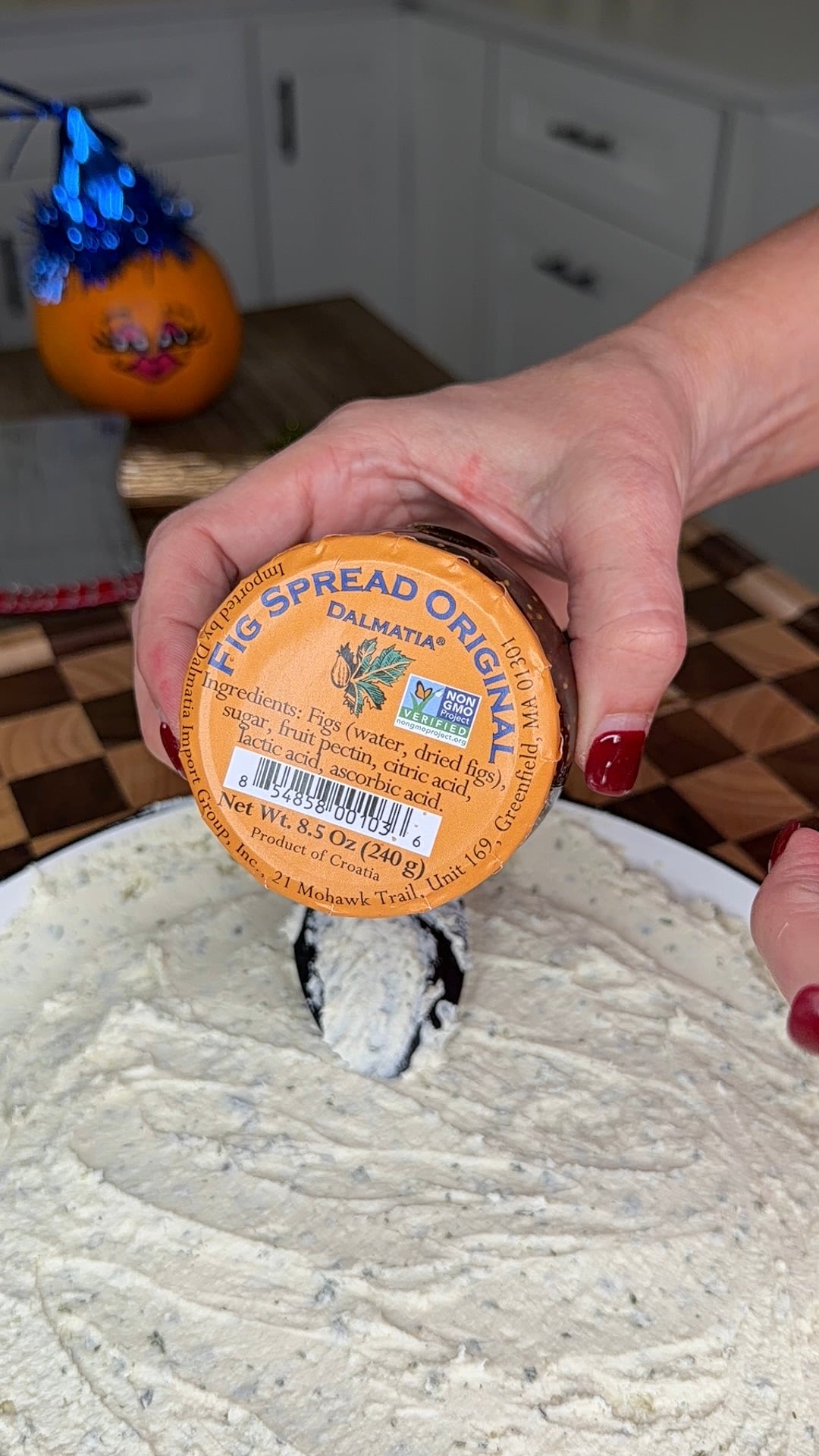 A hand holding a jar of Dalmatia Fig Spread over a bowl of creamy dip.