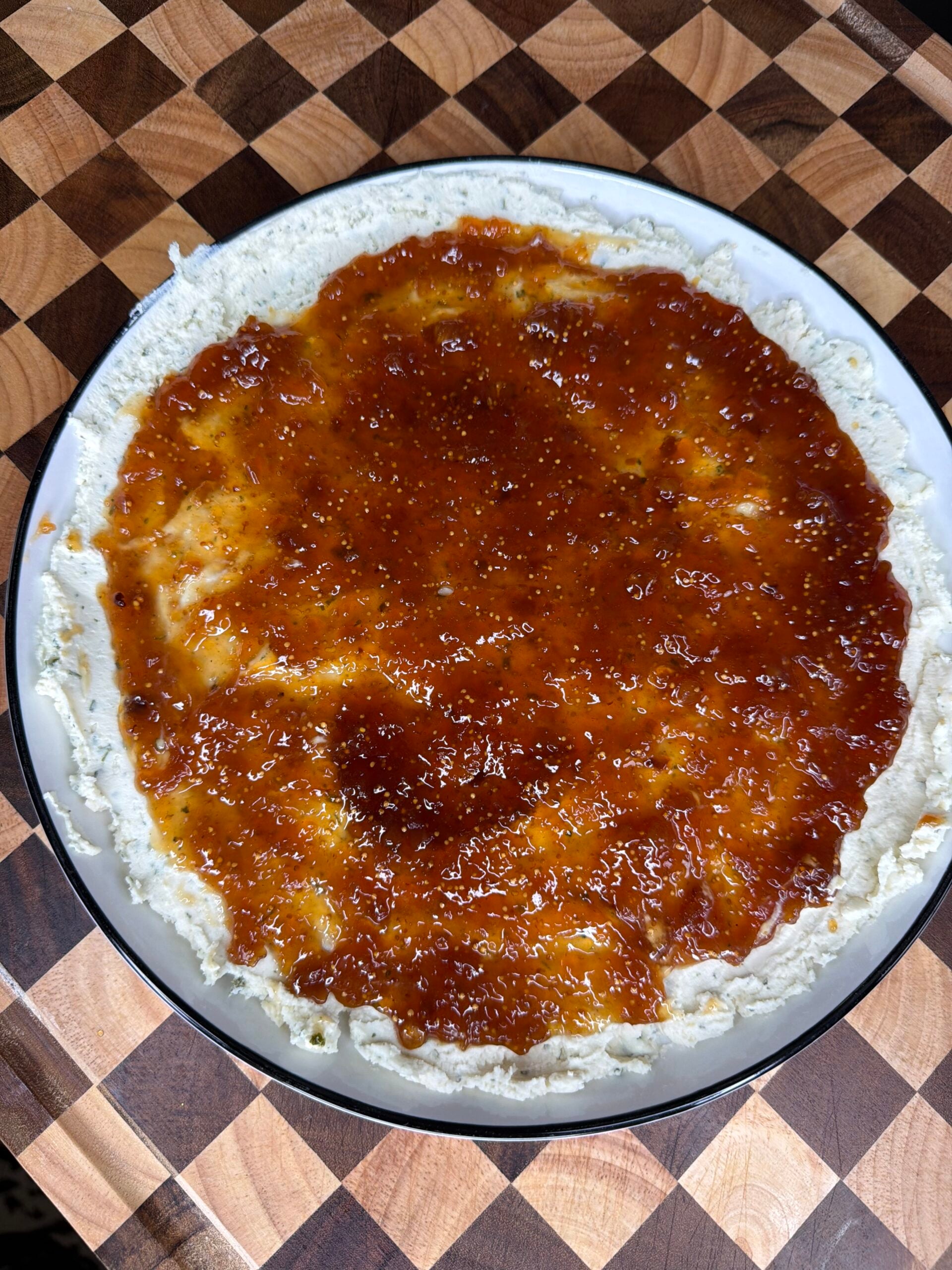 A round dish featuring a spread of white cheese topped with a layer of amber-colored jam.