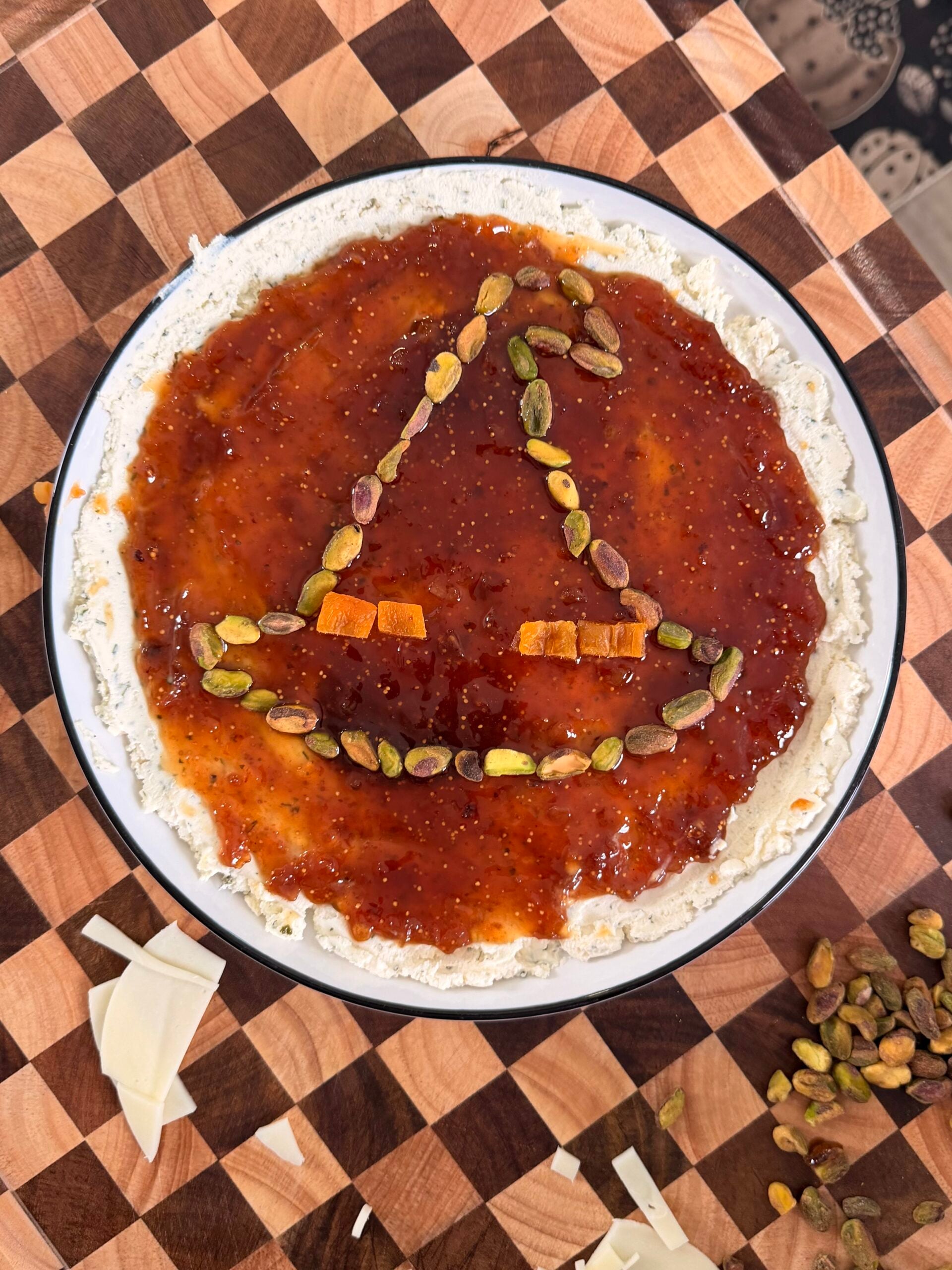 A round dish of fig jam and cheese arranged to look like a witchs hat using pistachio and dried fruit pieces.