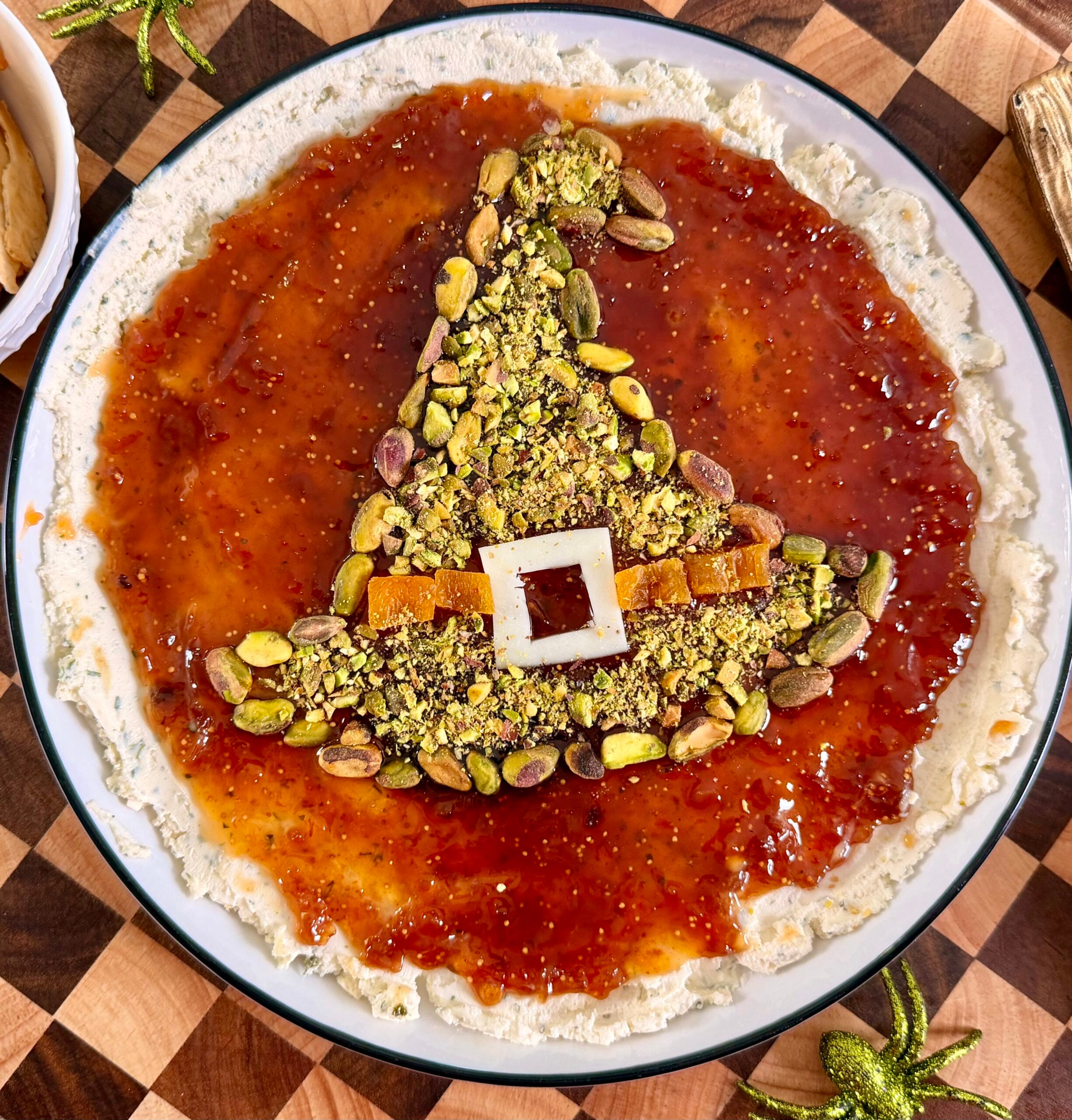 A witchs hat shape made of pistachios and dried fruit sits in the center of a round spread topped with red jam.
