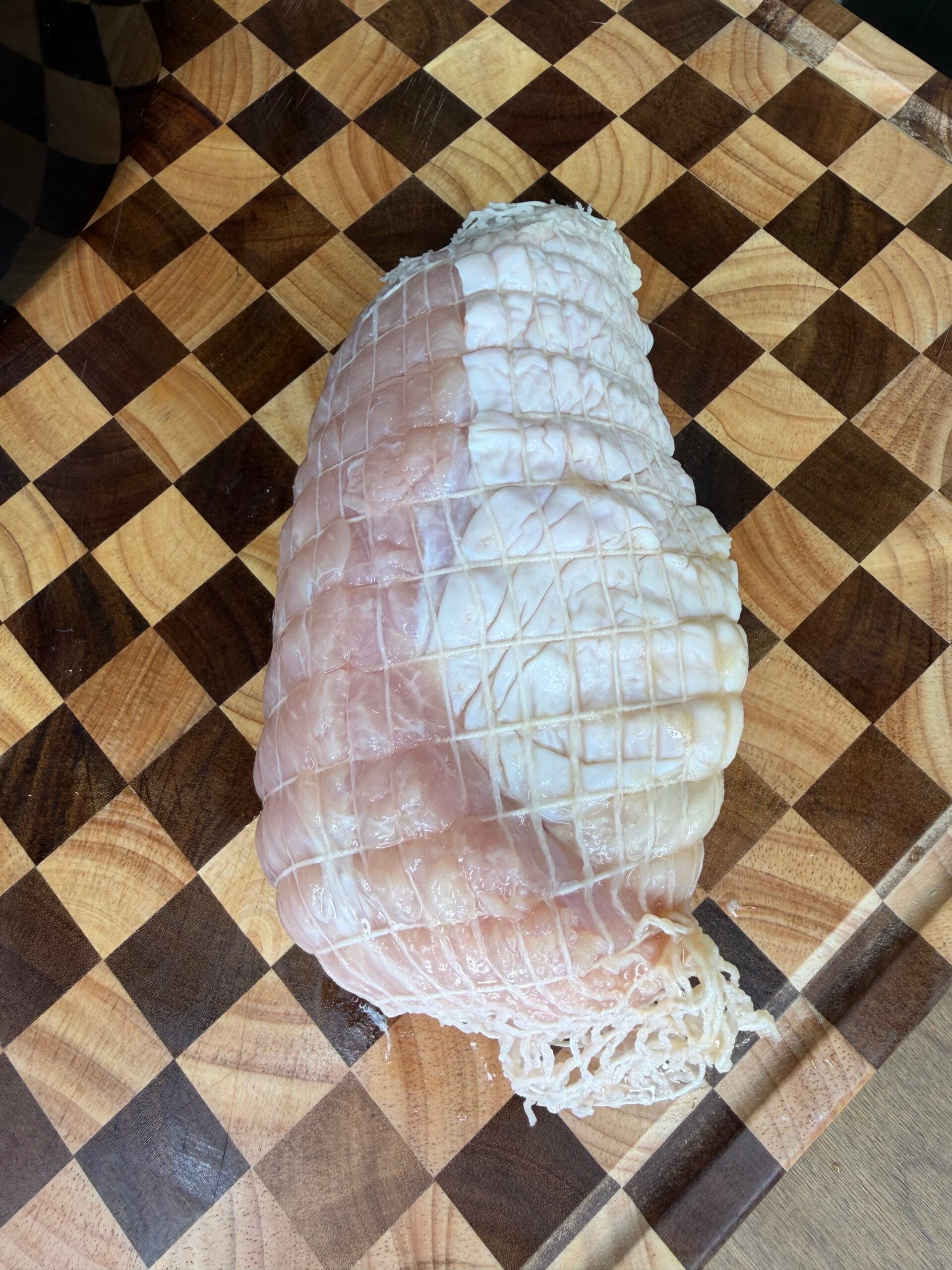 A raw, netted turkey breast on a checkered wooden cutting board.