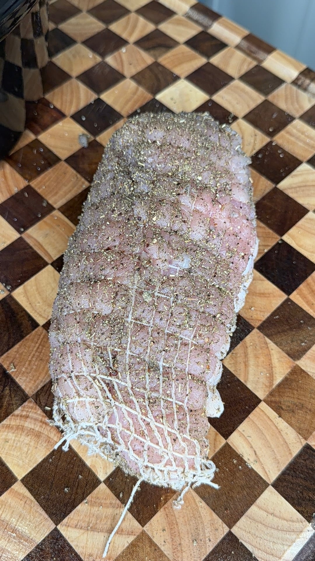 A seasoned, netting-covered roast on a checkered cutting board.