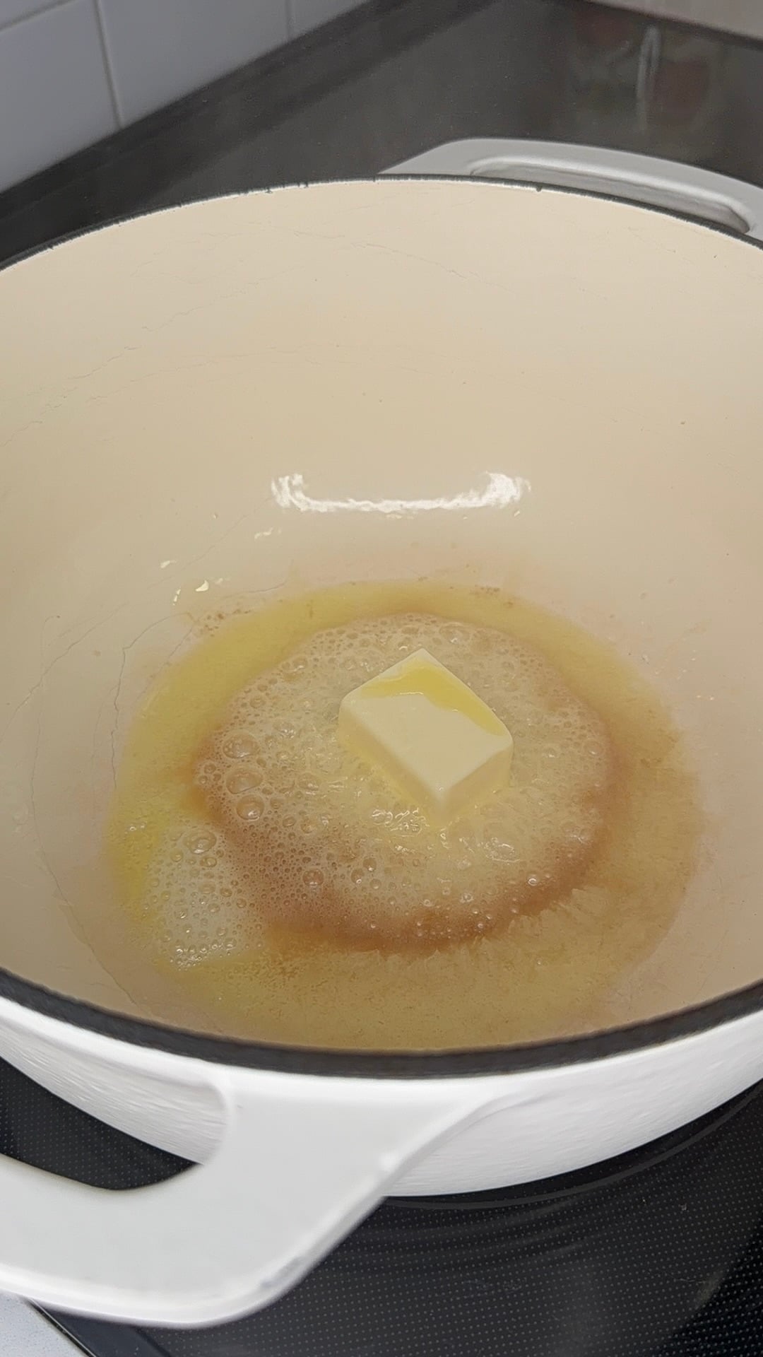 A square of butter melting in the bottom of a white pot on a stovetop.