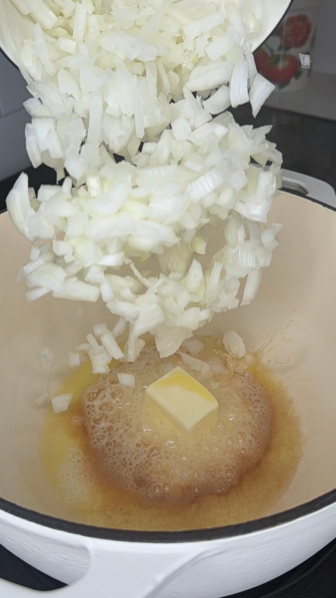 Chopped white onions being poured into a pot containing a melting pat of butter.
