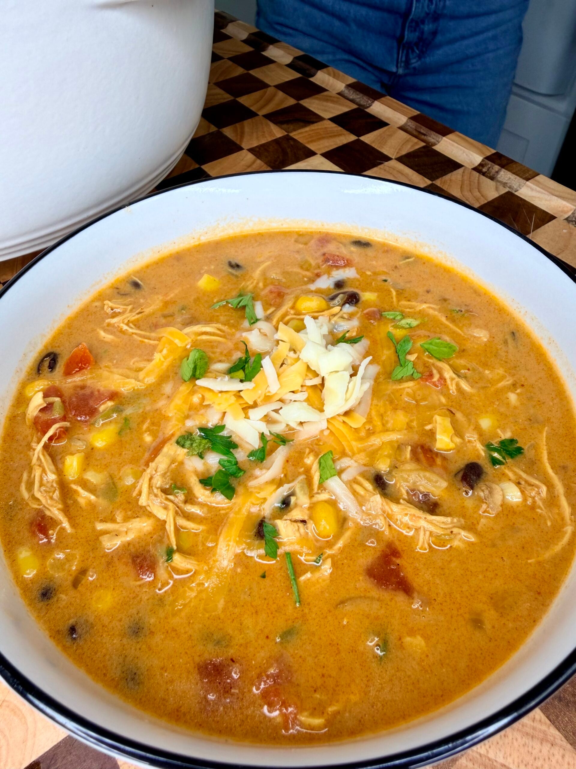 A bowl of creamy chicken tortilla soup topped with shredded cheese and cilantro.