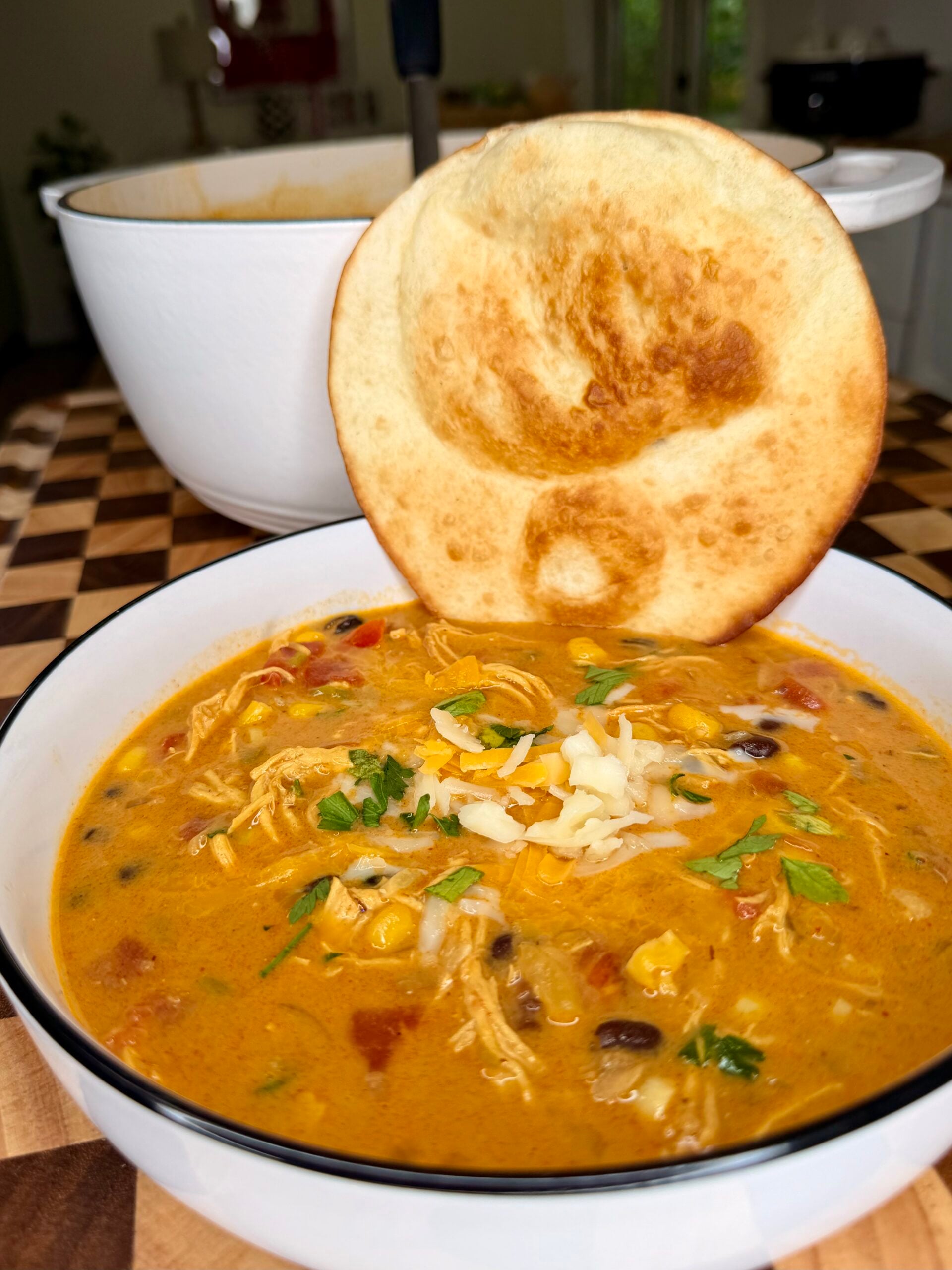 A bowl of chicken tortilla soup topped with shredded cheese and cilantro, served with a round crispy flatbread.