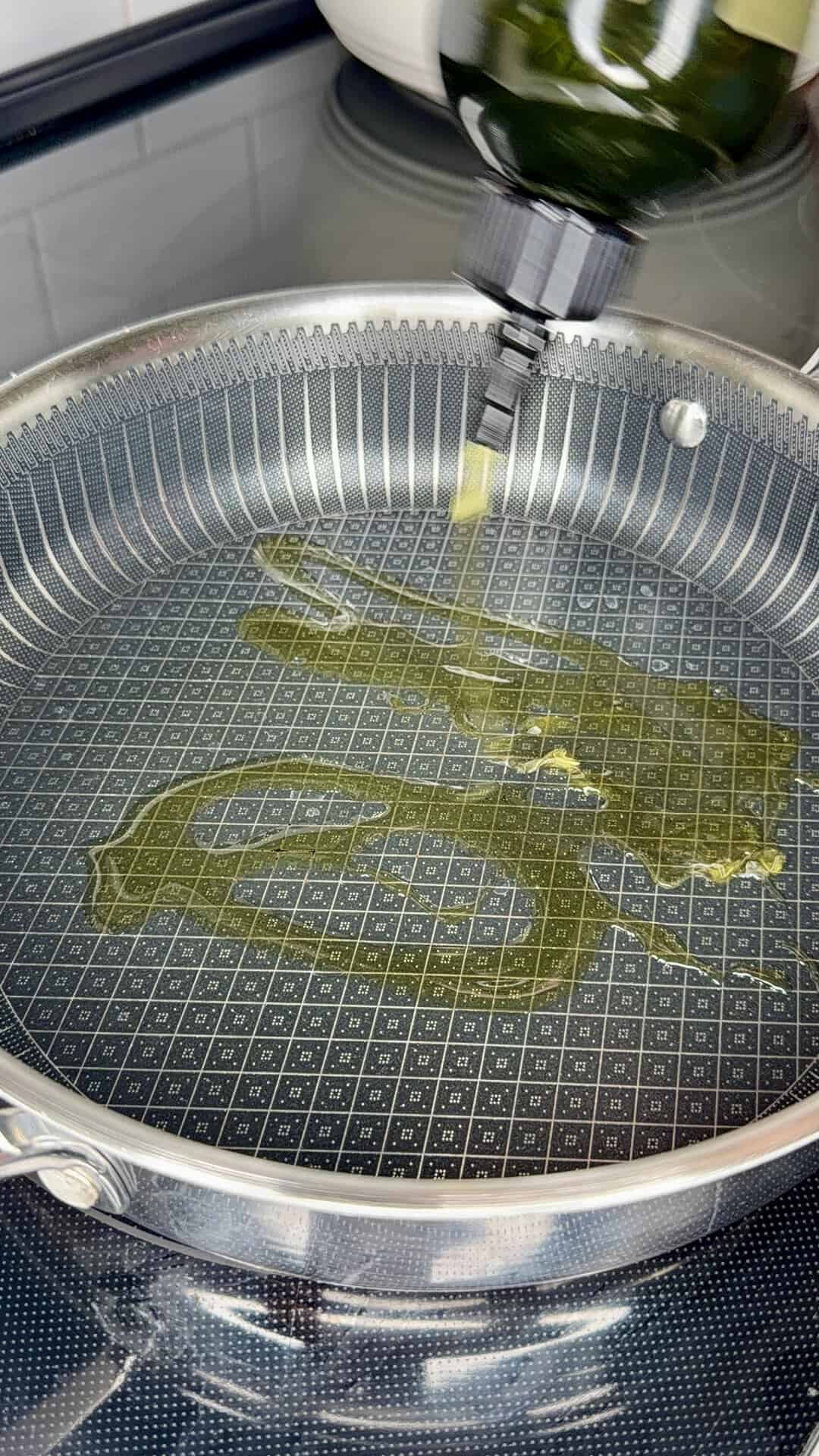Olive oil being poured from a bottle into a textured nonstick frying pan.