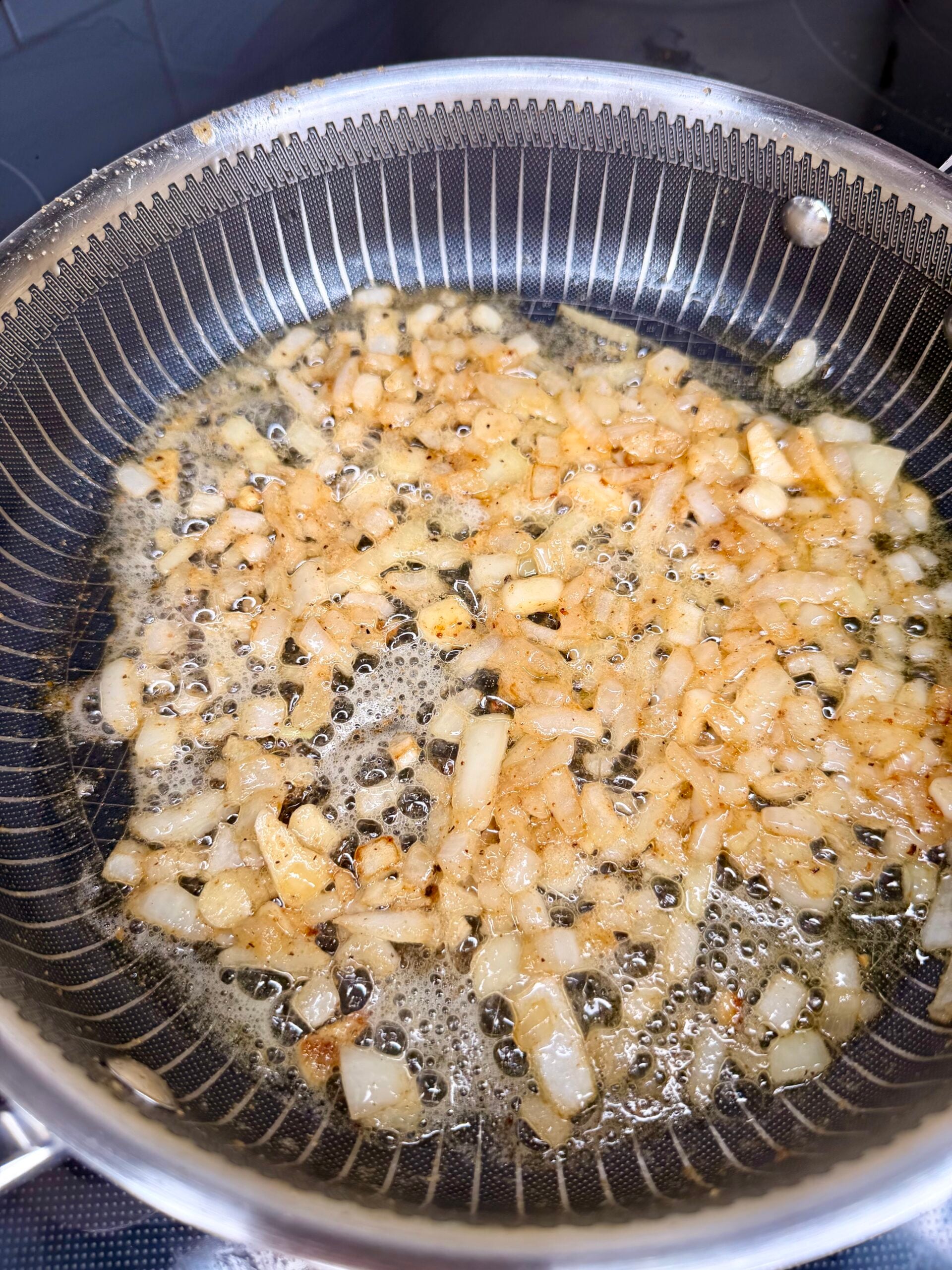 Diced onions sautéing in a textured metal skillet.