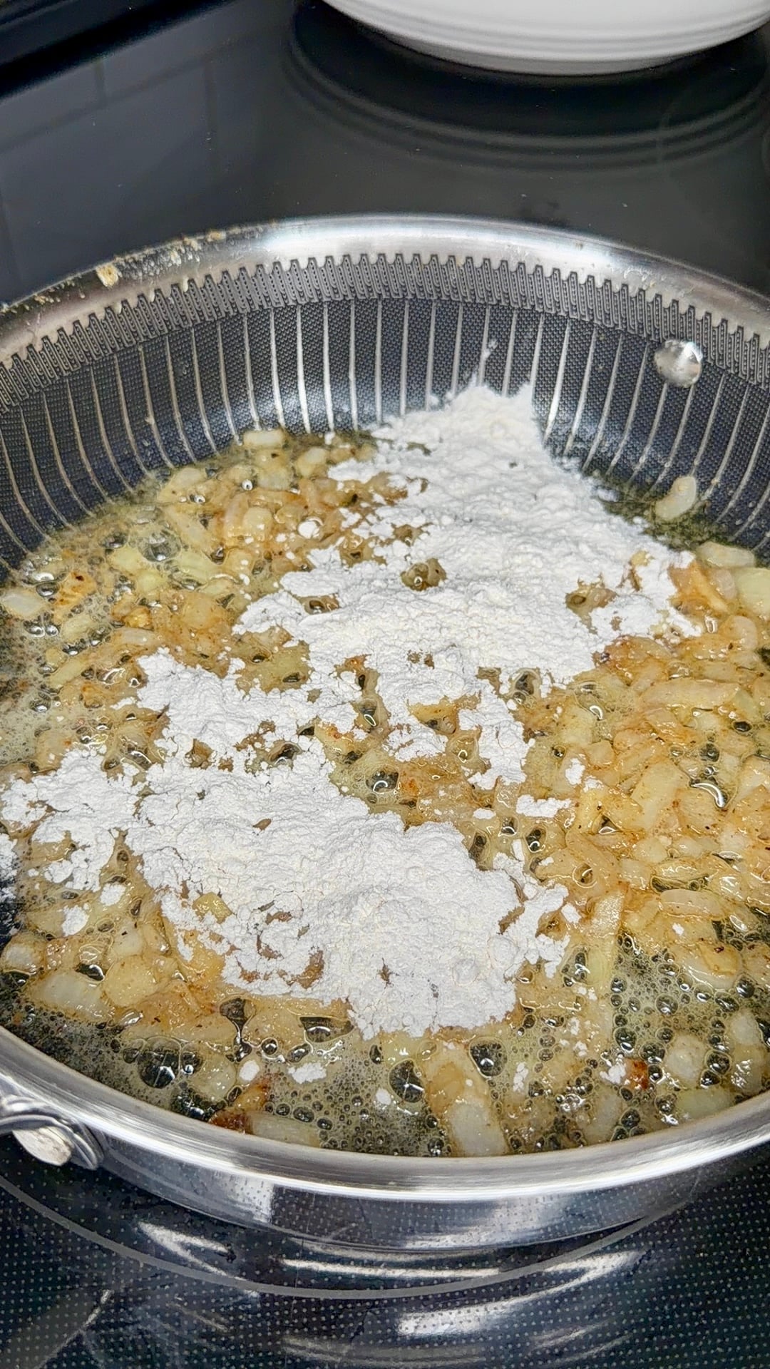 Flour sprinkled over diced onions sizzling in a frying pan.