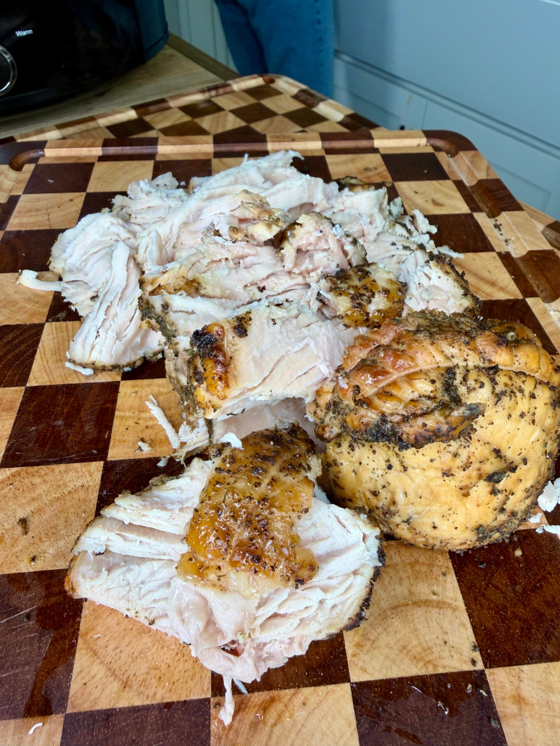 Sliced herb-crusted roasted turkey breast on a checkered wooden cutting board.