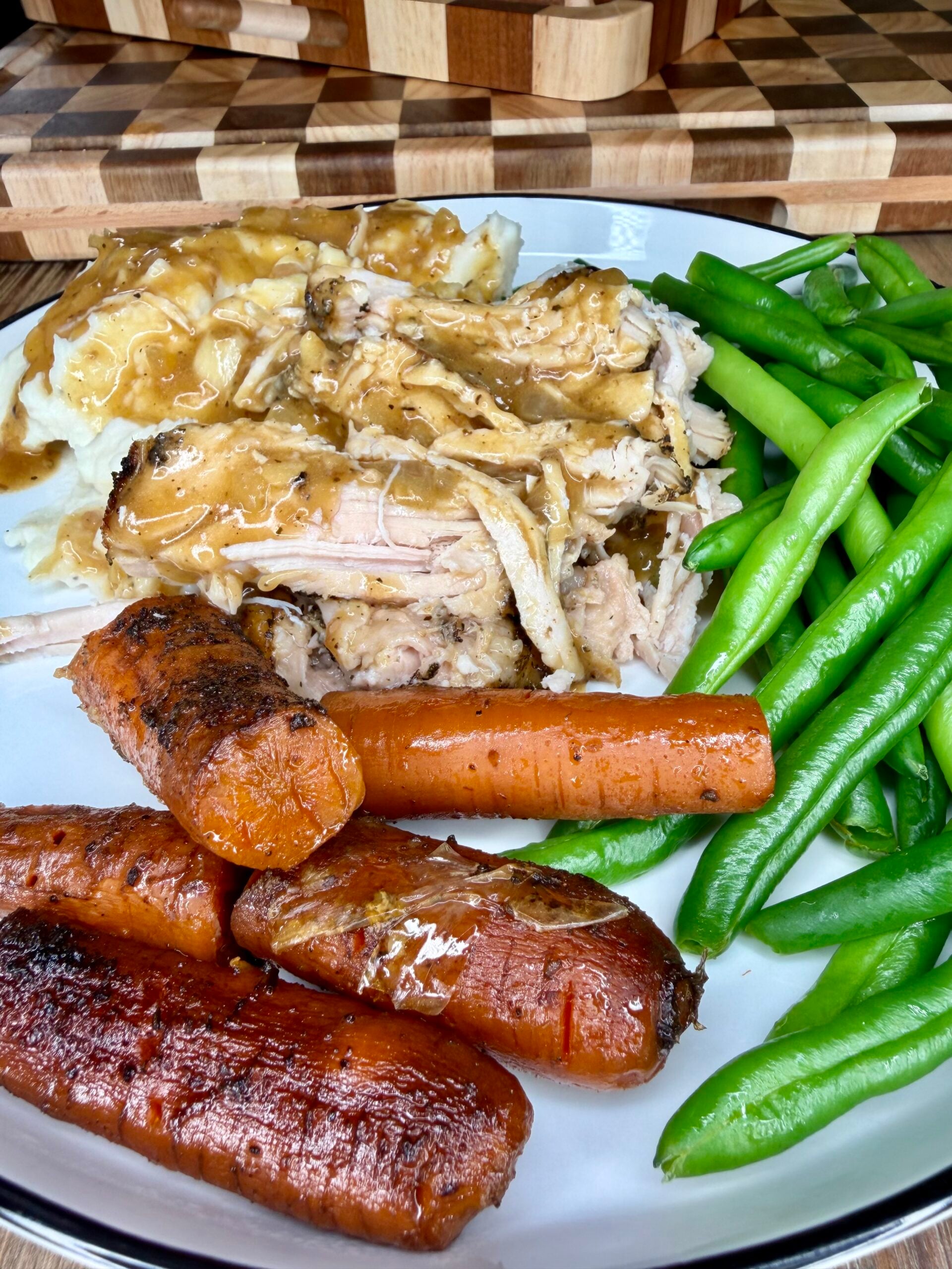 A plate of roasted chicken with gravy, mashed potatoes, glazed carrots, and steamed green beans.