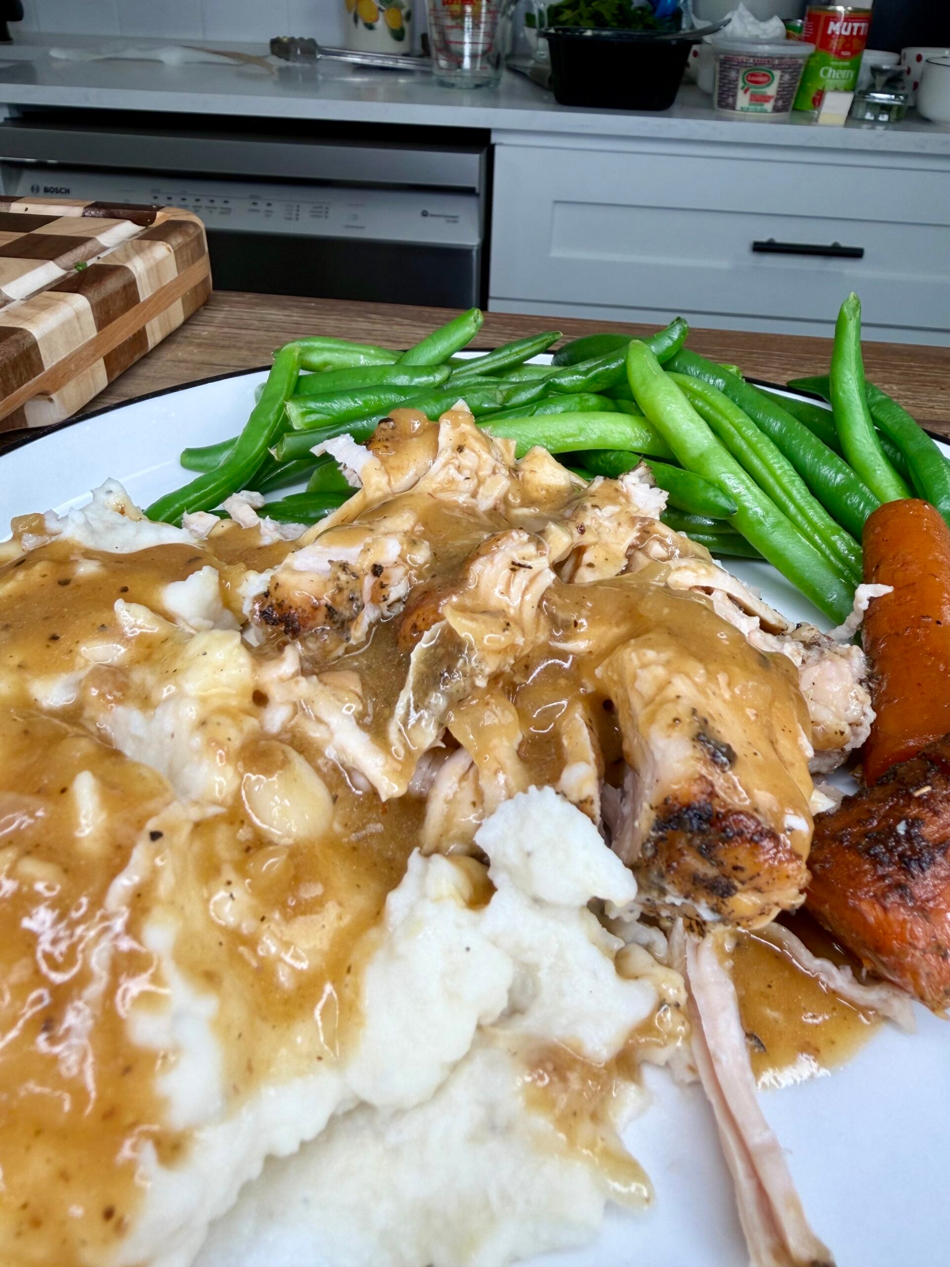 A plate of roasted chicken with gravy, mashed potatoes, green beans, and a roasted carrot.