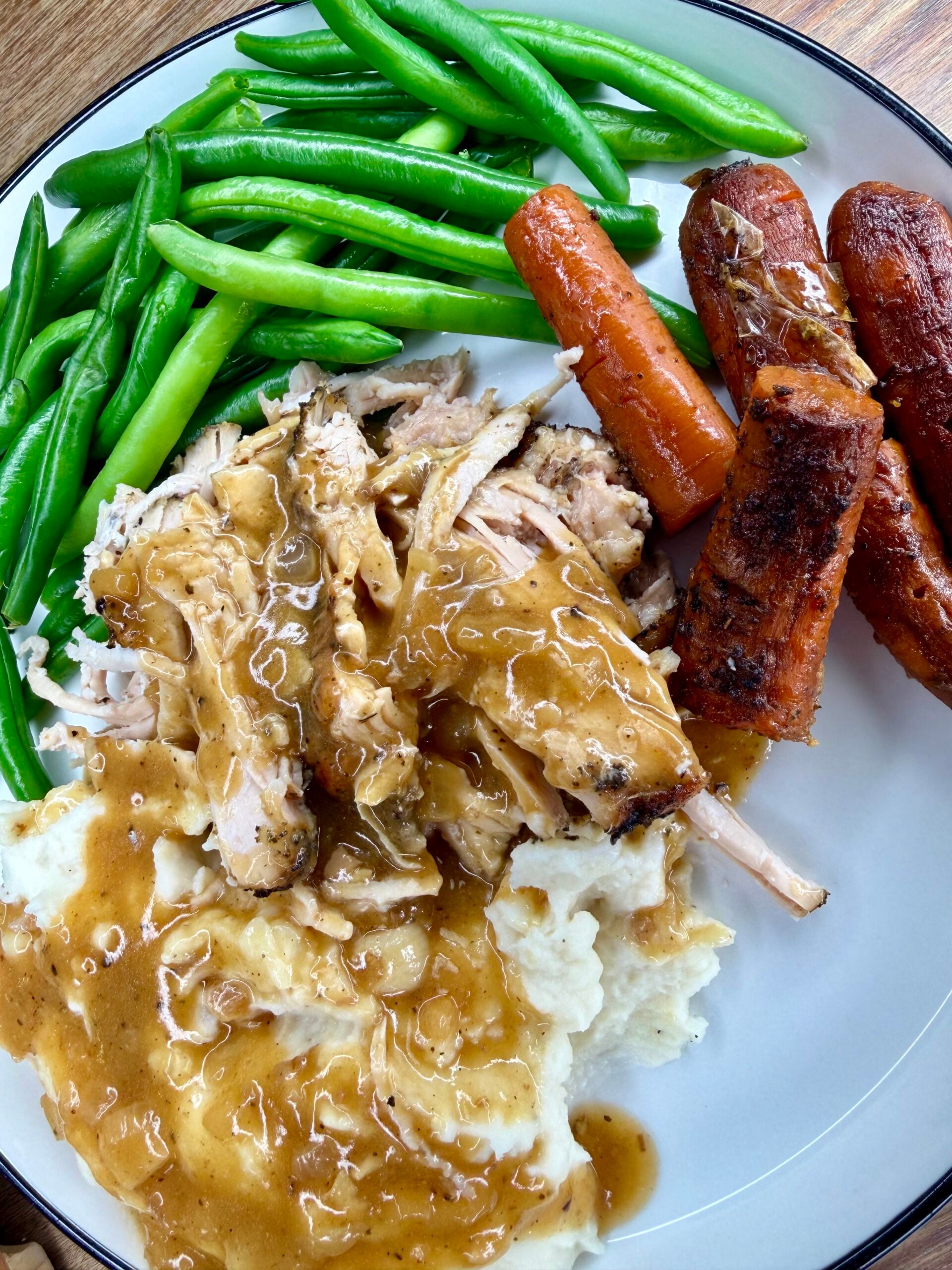 A plate of roast chicken and mashed potatoes covered in gravy, served with green beans and roasted carrots.