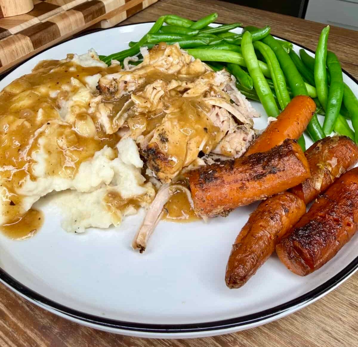 A plate of roasted chicken and mashed potatoes covered in gravy, served with green beans and roasted carrots.