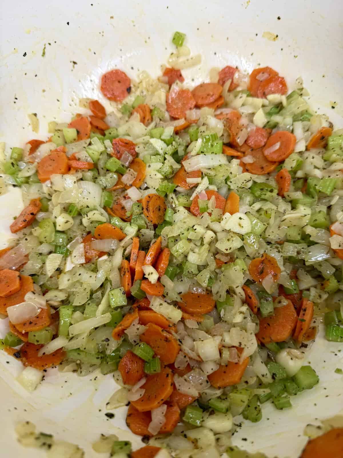 A mixture of sautéed chopped carrots, celery, and onions seasoned with herbs in a large white bowl.