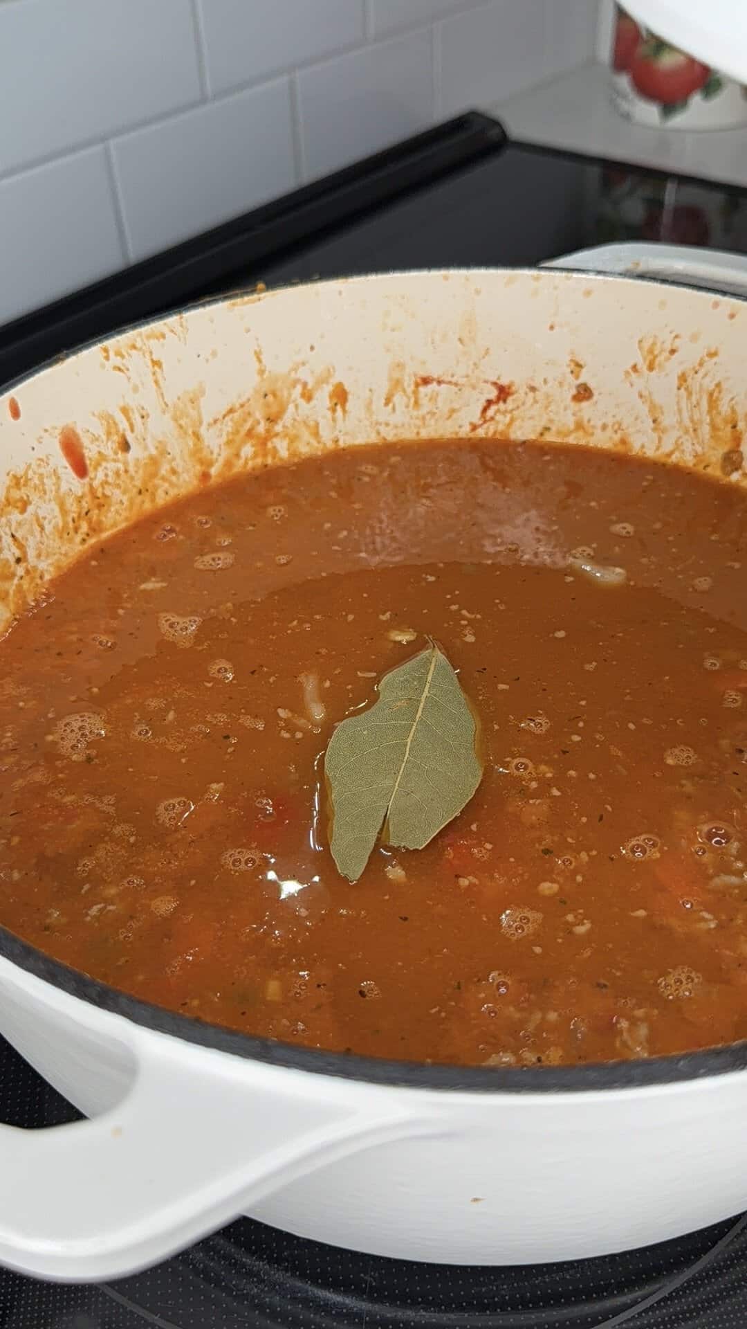 A single bay leaf floats in a large pot of simmering tomato-based sauce.