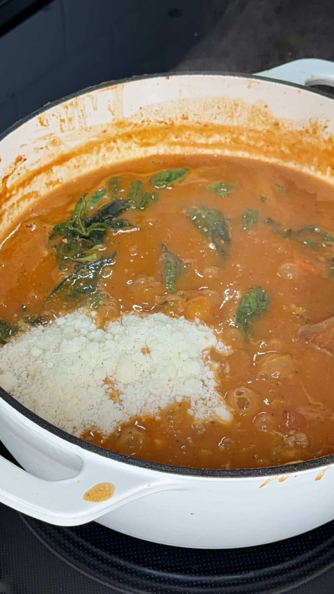 A pot of tomato sauce simmering with basil leaves and a mound of grated cheese.