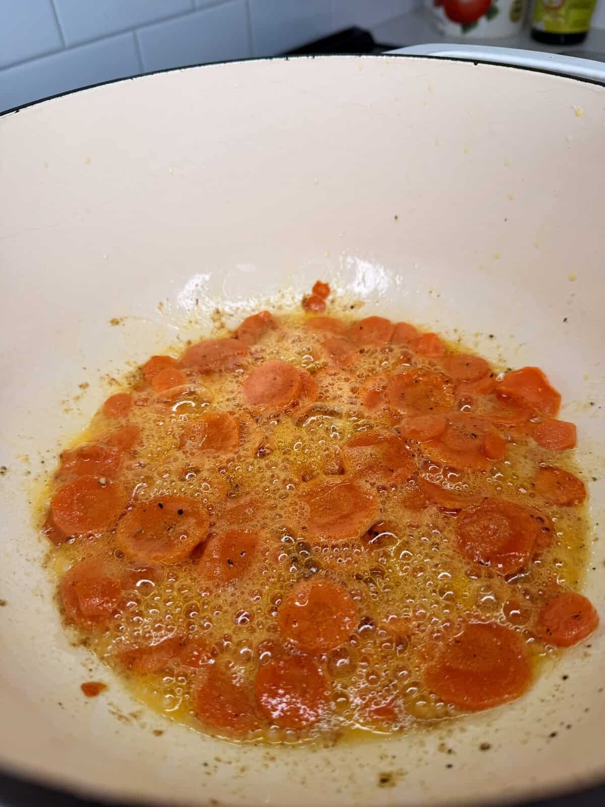 Sliced carrots sautéing in bubbling oil in a light-colored enameled pot.