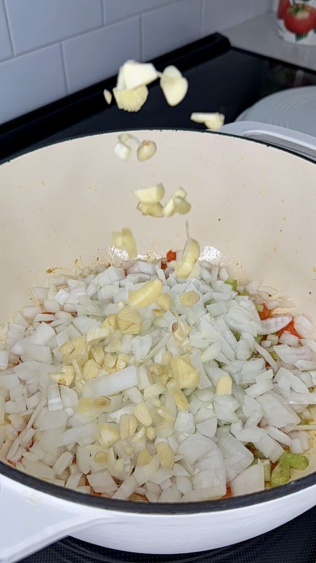 Chopped garlic falls into a pot filled with diced onions and vegetables.