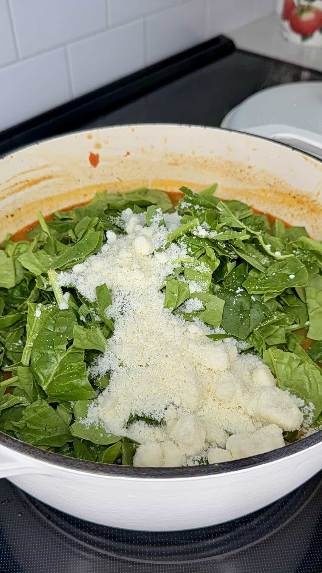 A pot of tomato-based sauce topped with a mound of fresh spinach and grated parmesan cheese.