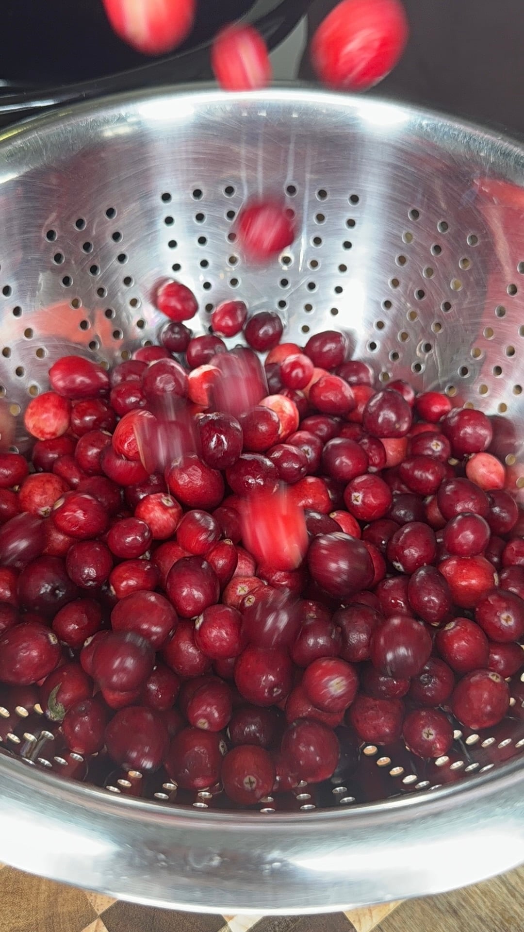 Fresh cranberries falling into a stainless steel colander.