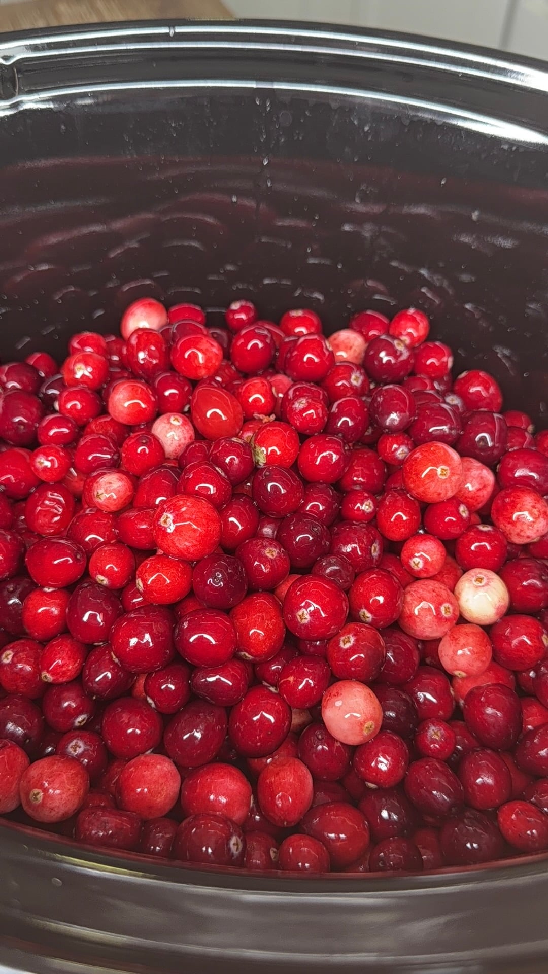 A large pile of fresh red cranberries inside a black slow cooker.