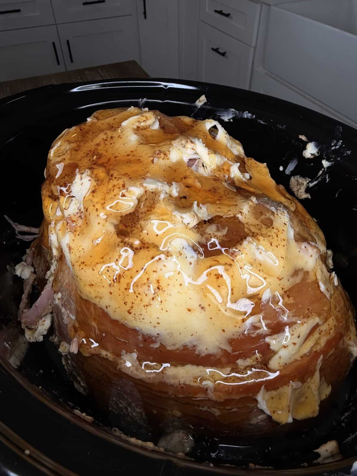 A glazed ham topped with melted cheese in a slow cooker.