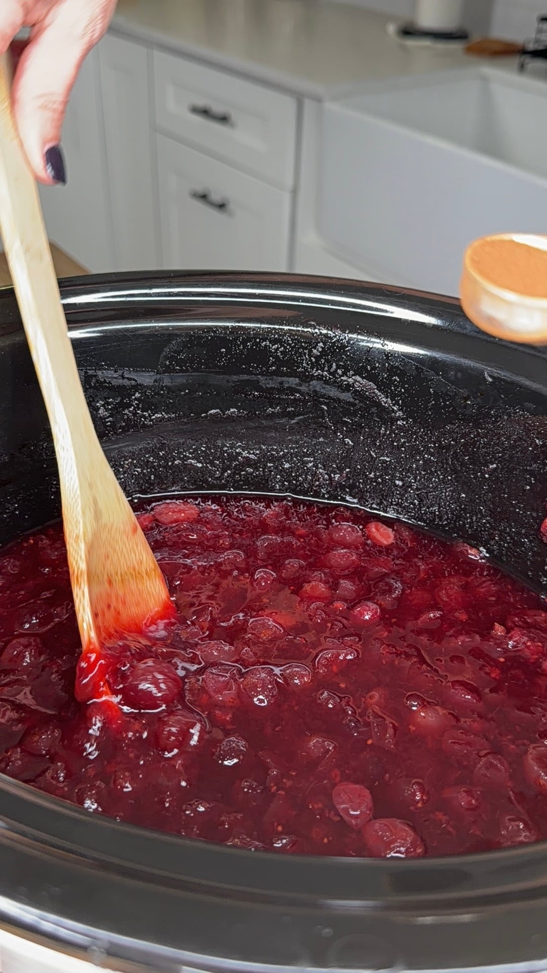 A wooden spoon stirs a simmering mixture of cranberries in a slow cooker.