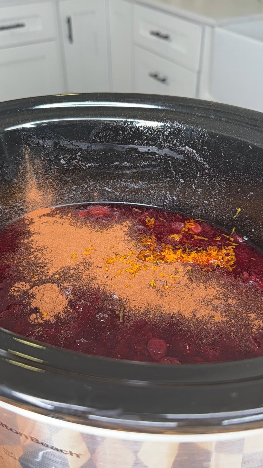 Cranberry sauce simmering in a slow cooker, topped with a dusting of ground cinnamon and orange zest.