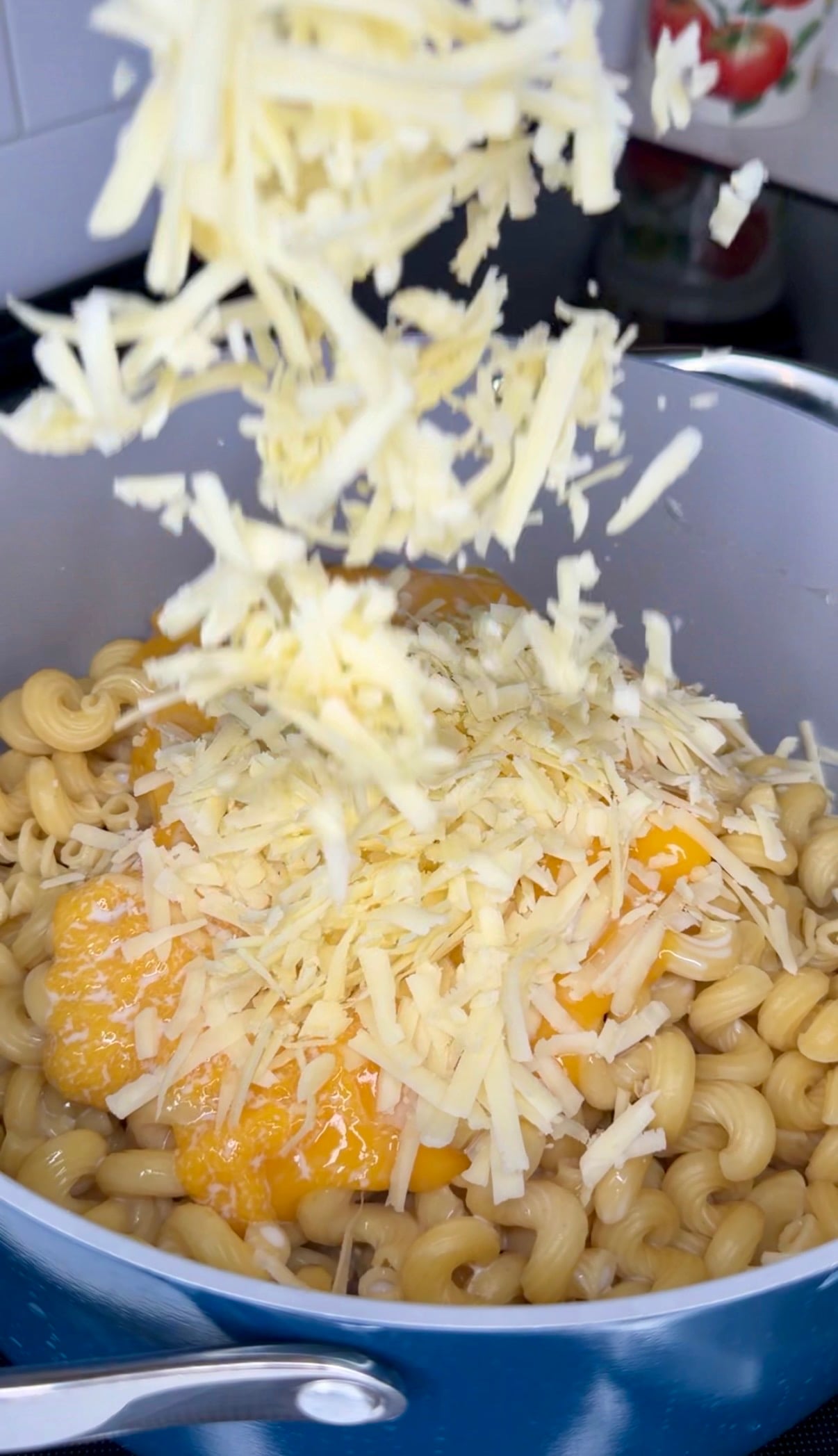 Shredded cheese being sprinkled into a pot of cooked pasta with sauce.