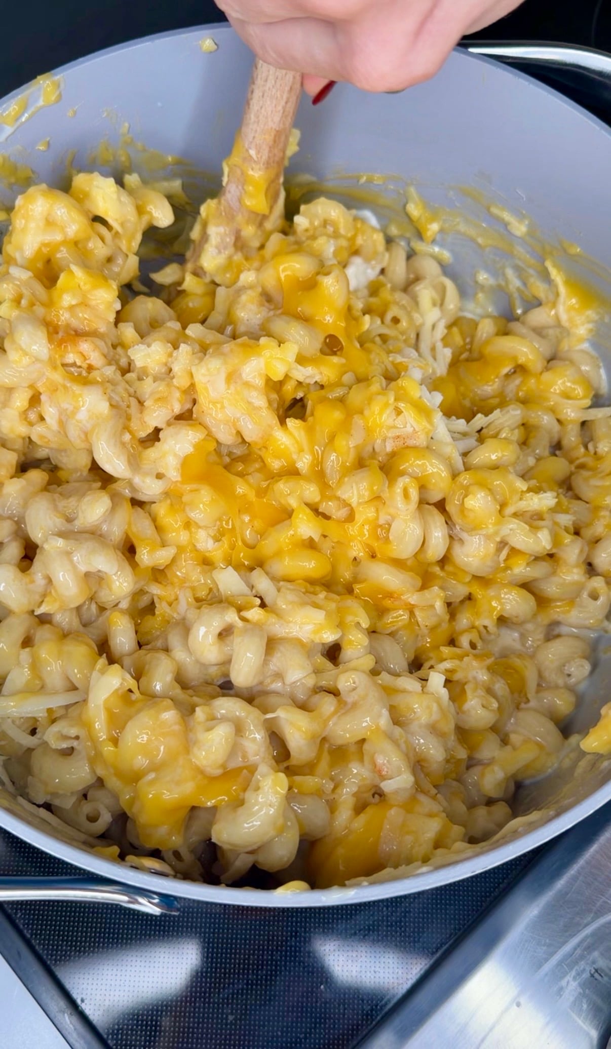 A person uses a wooden spoon to stir melted cheese into a pot of macaroni.