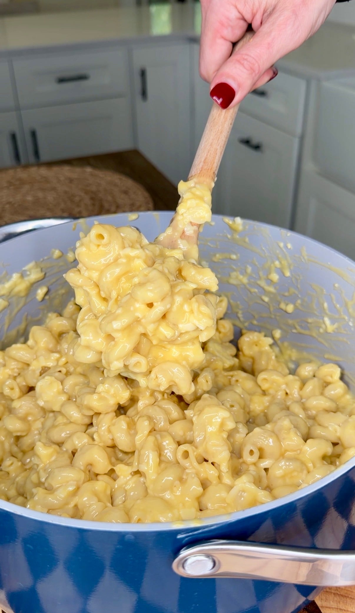 A wooden spoon lifts a scoop of creamy macaroni and cheese from a blue pot.