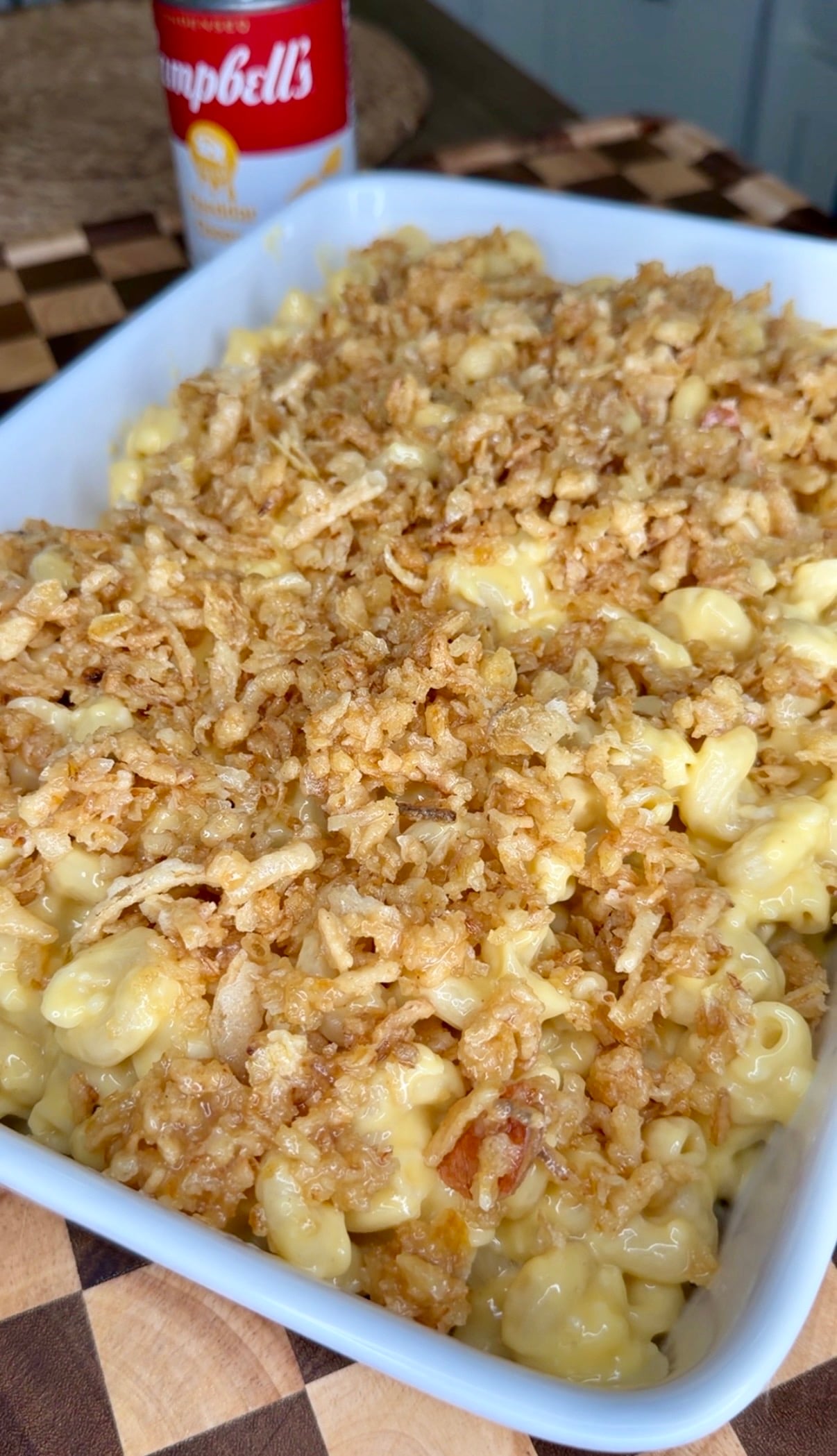 A white baking dish filled with macaroni and cheese topped with crispy fried onions, with a can of Campbells soup in the background.