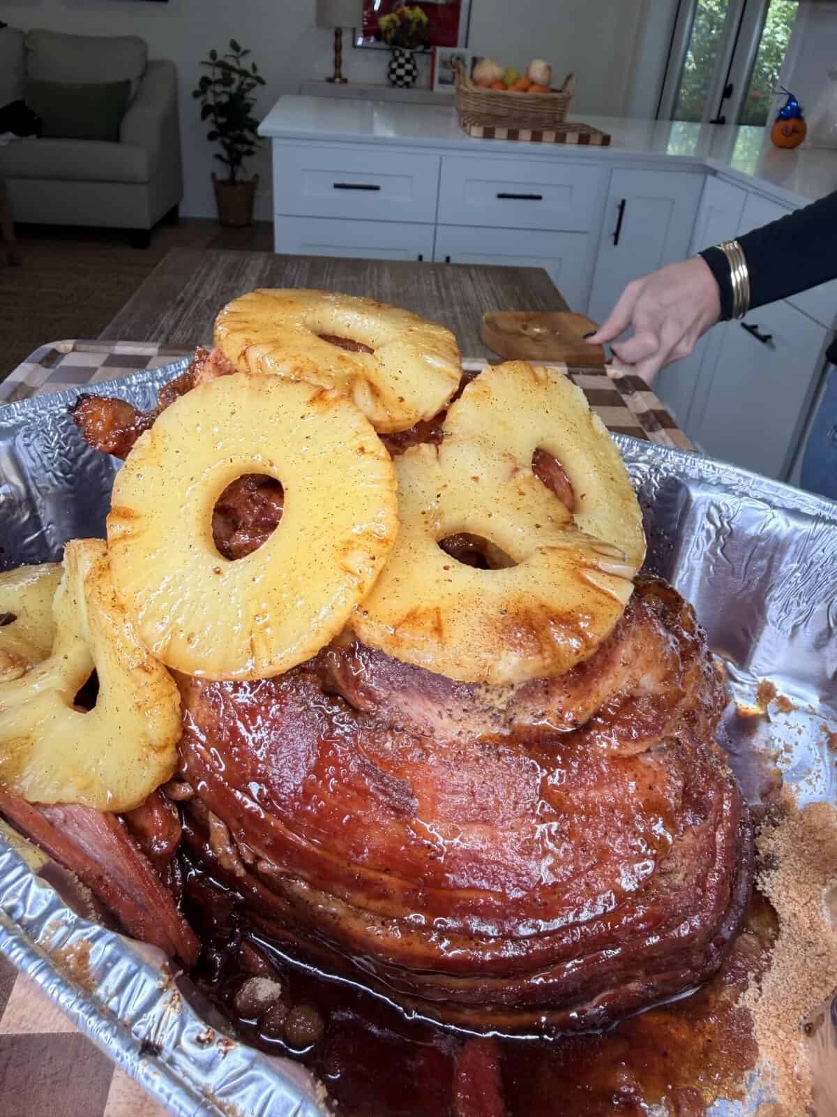 A glazed ham topped with pineapple rings in a foil roasting pan.
