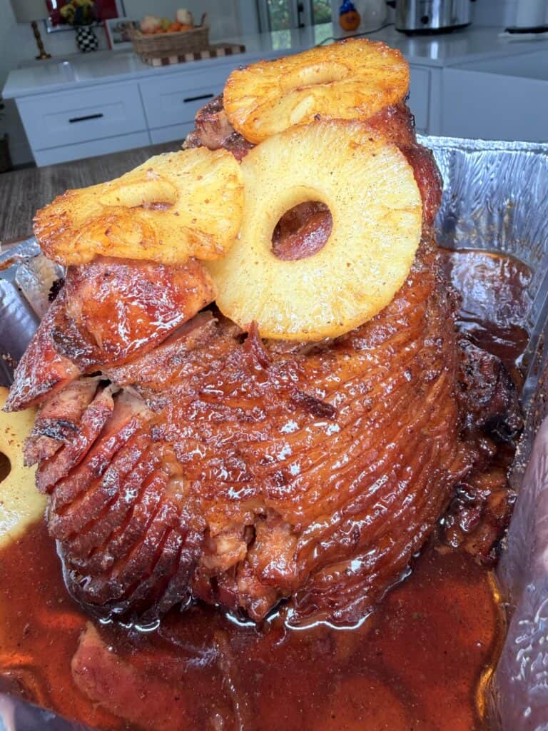 Glazed spiral-cut ham topped with pineapple rings in a foil roasting pan.