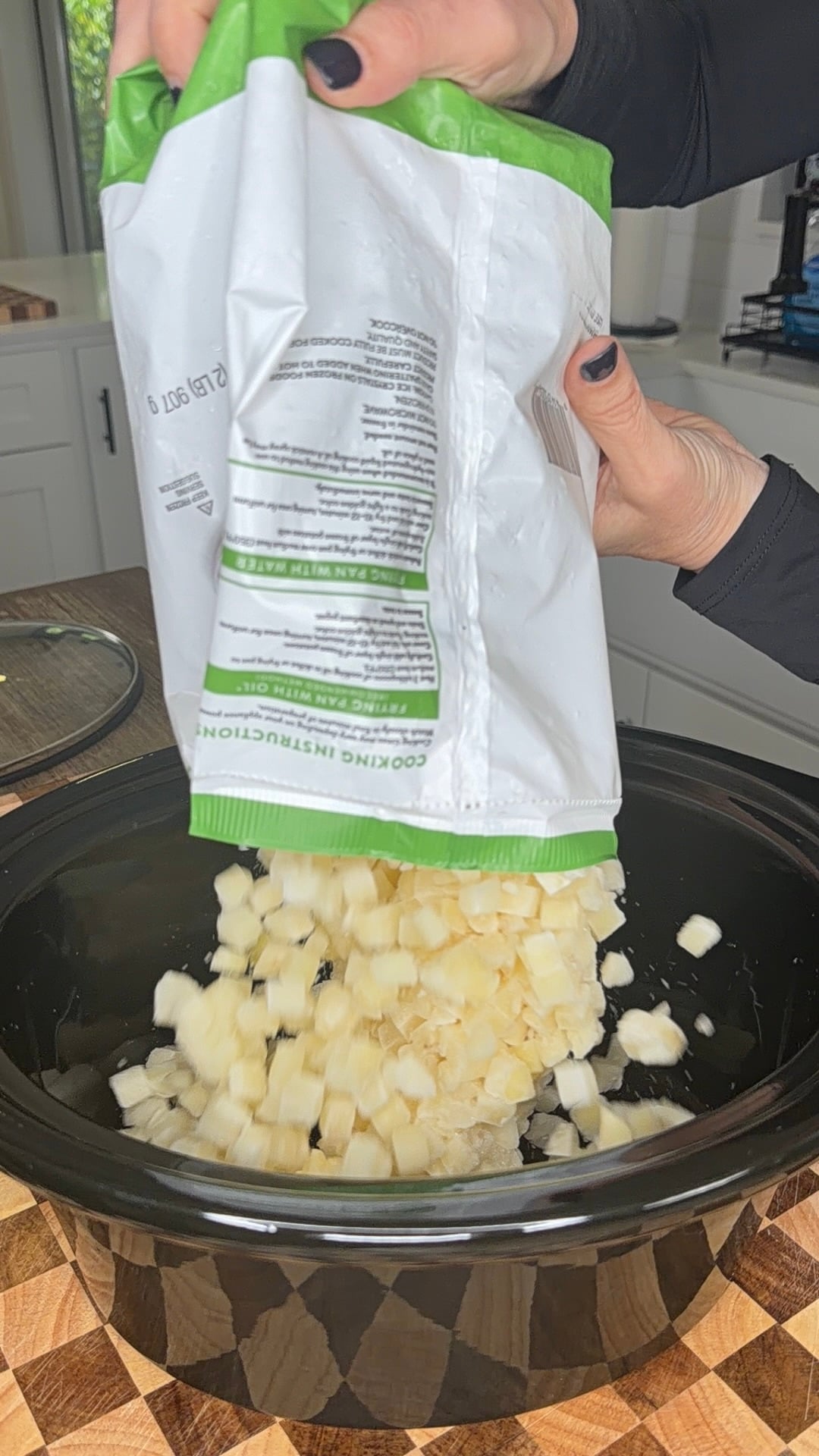 Hands pouring a bag of frozen diced potatoes into a slow cooker.