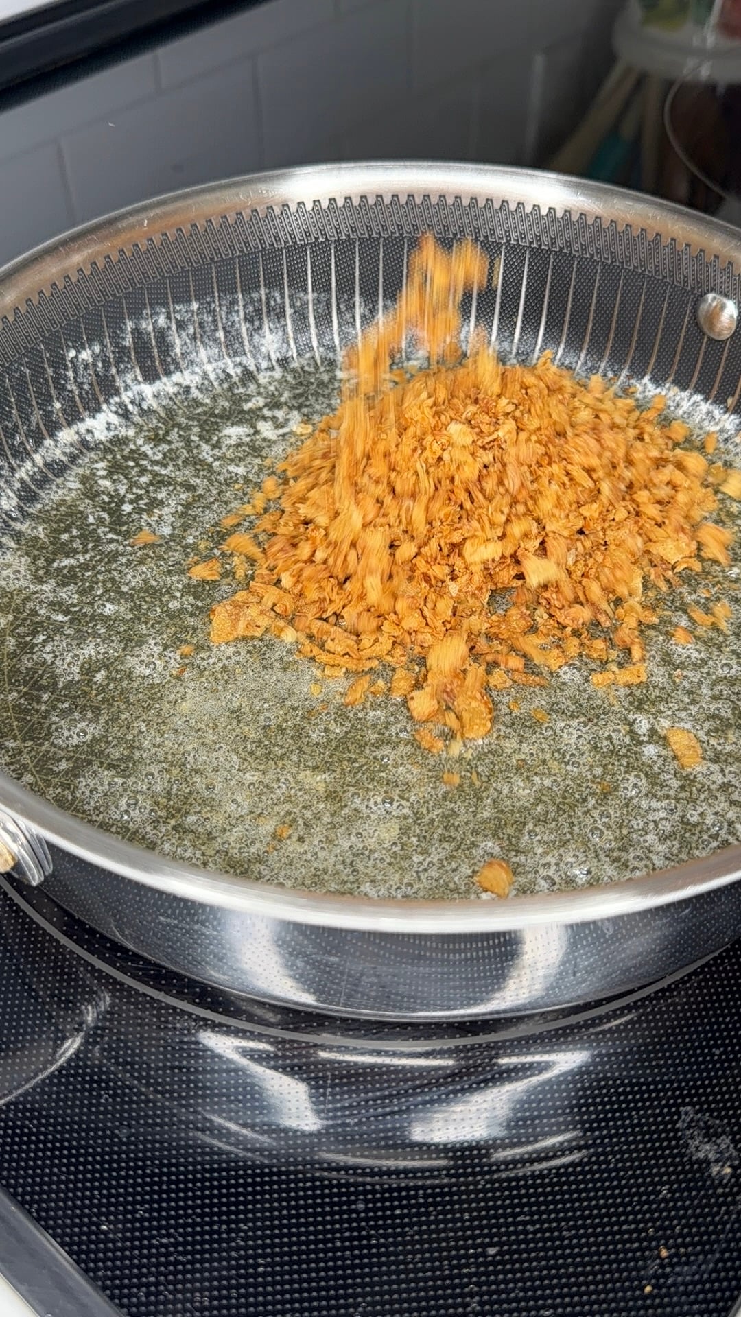 Crispy fried shallots being poured into a pan of melting butter.