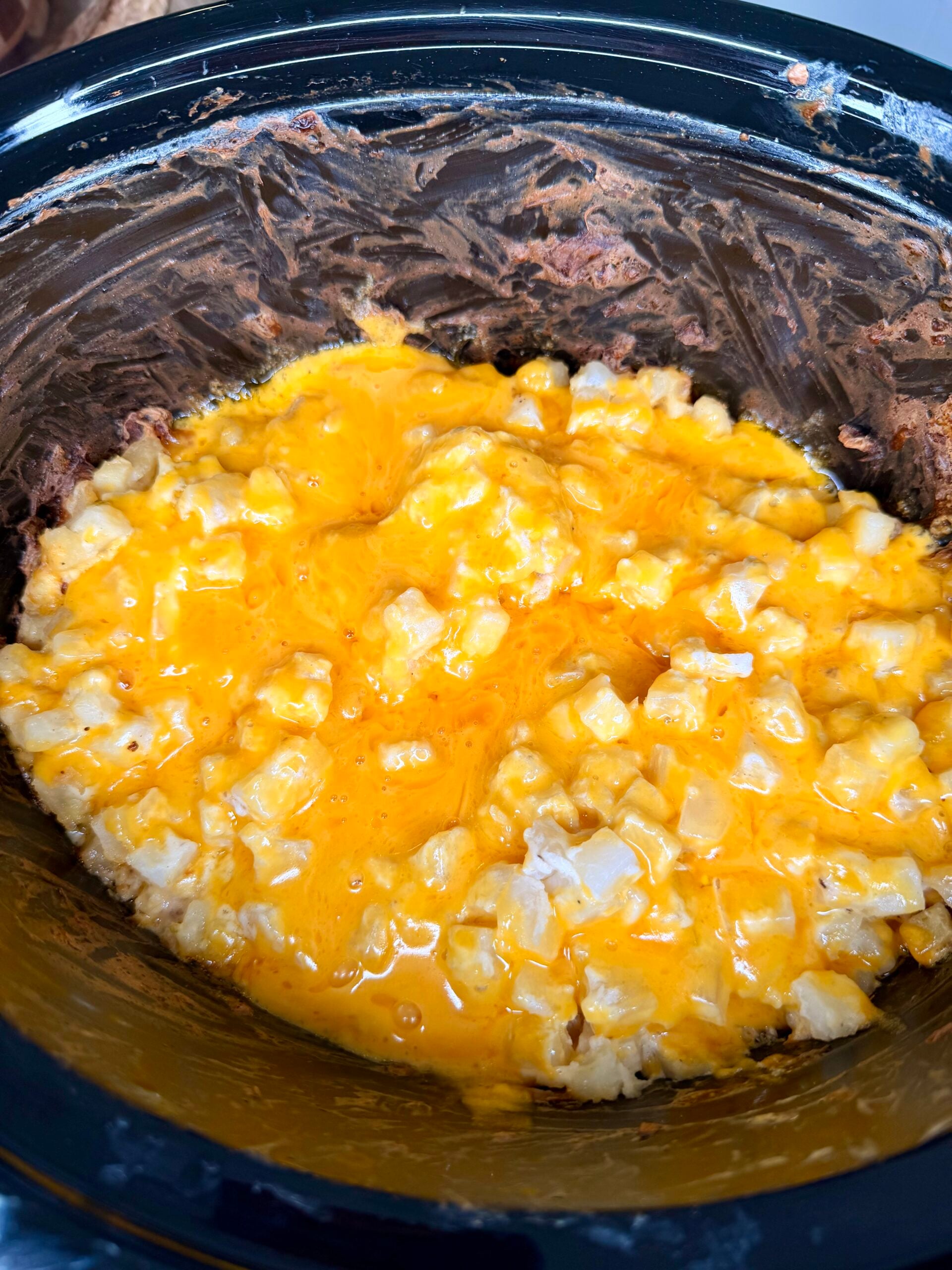 Diced potatoes topped with melted orange cheese in a slow cooker.