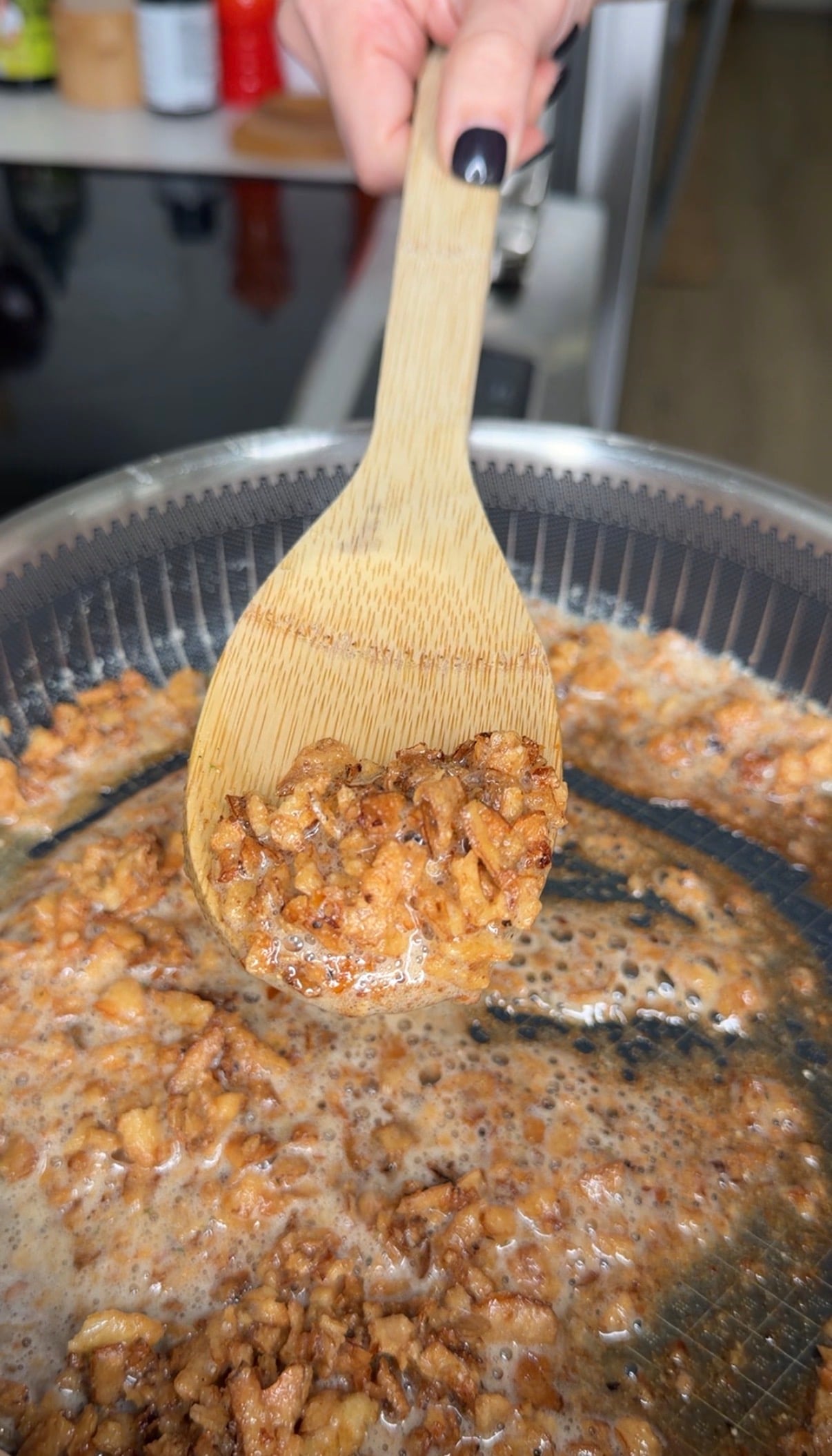 A wooden spoon lifts chopped, browned meat from a pan of sizzling fat.