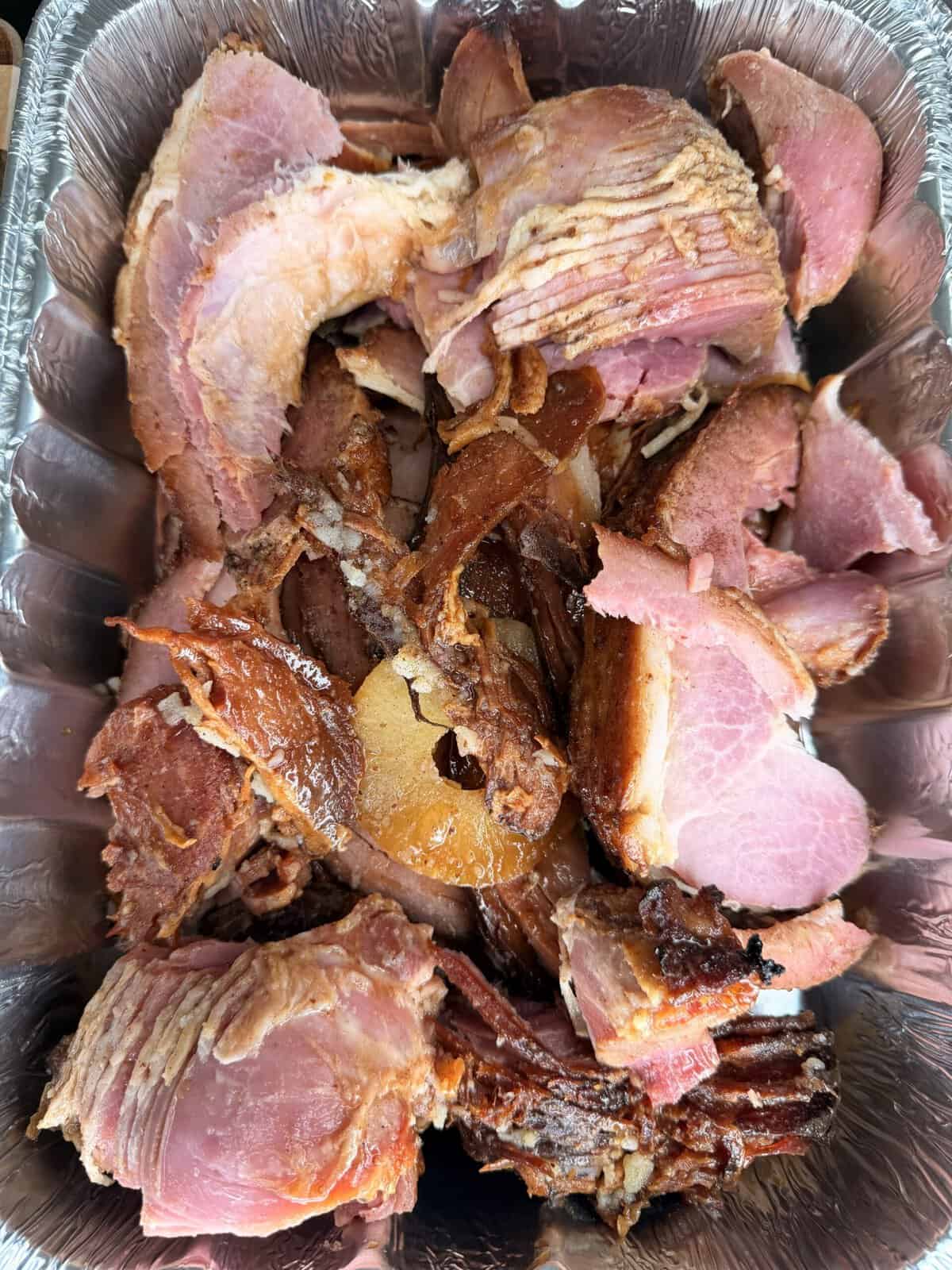 Sliced glazed ham with pineapple rings in a foil catering pan.