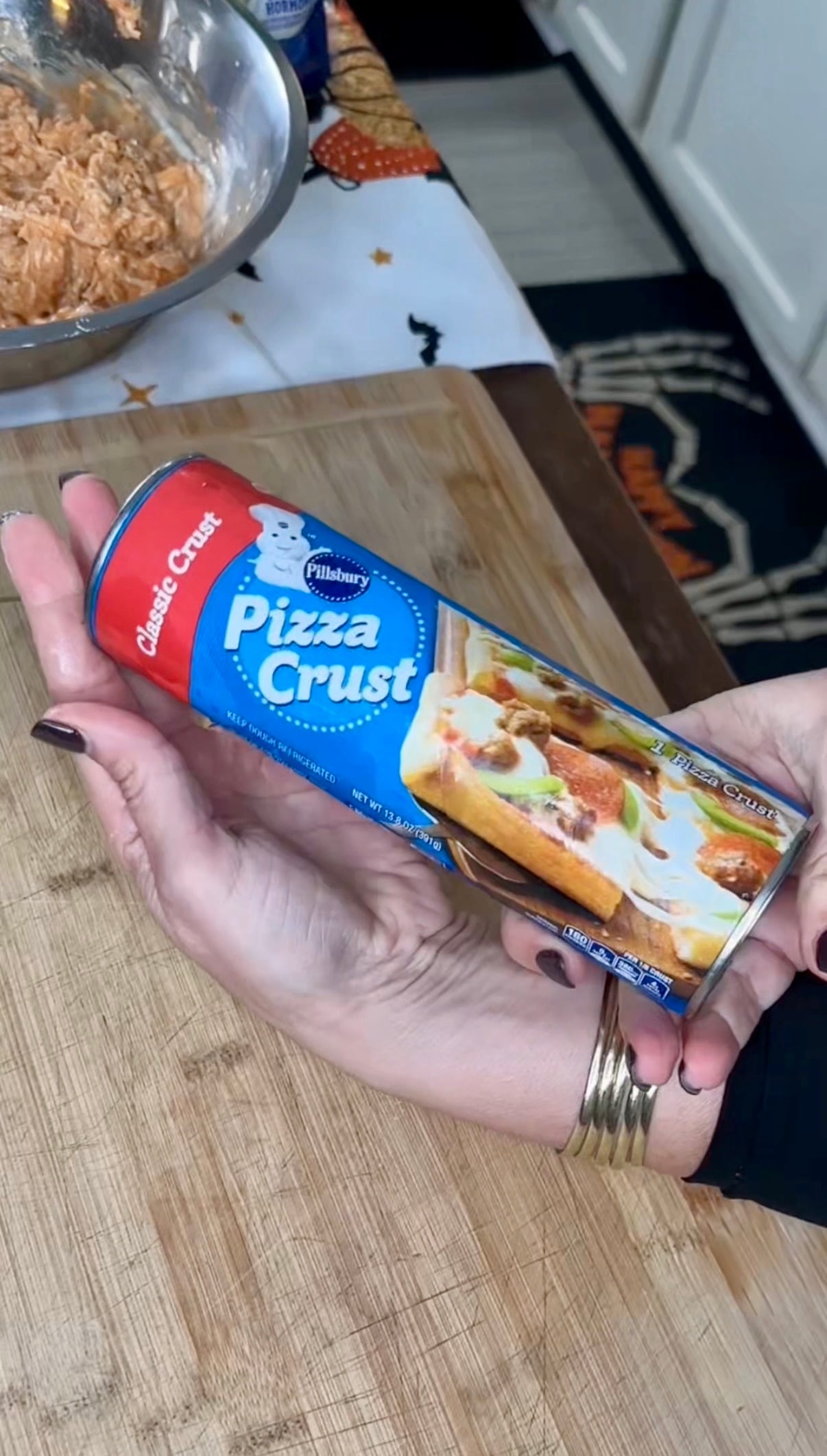 A person holding a cylindrical package of Pillsbury refrigerated classic pizza crust.