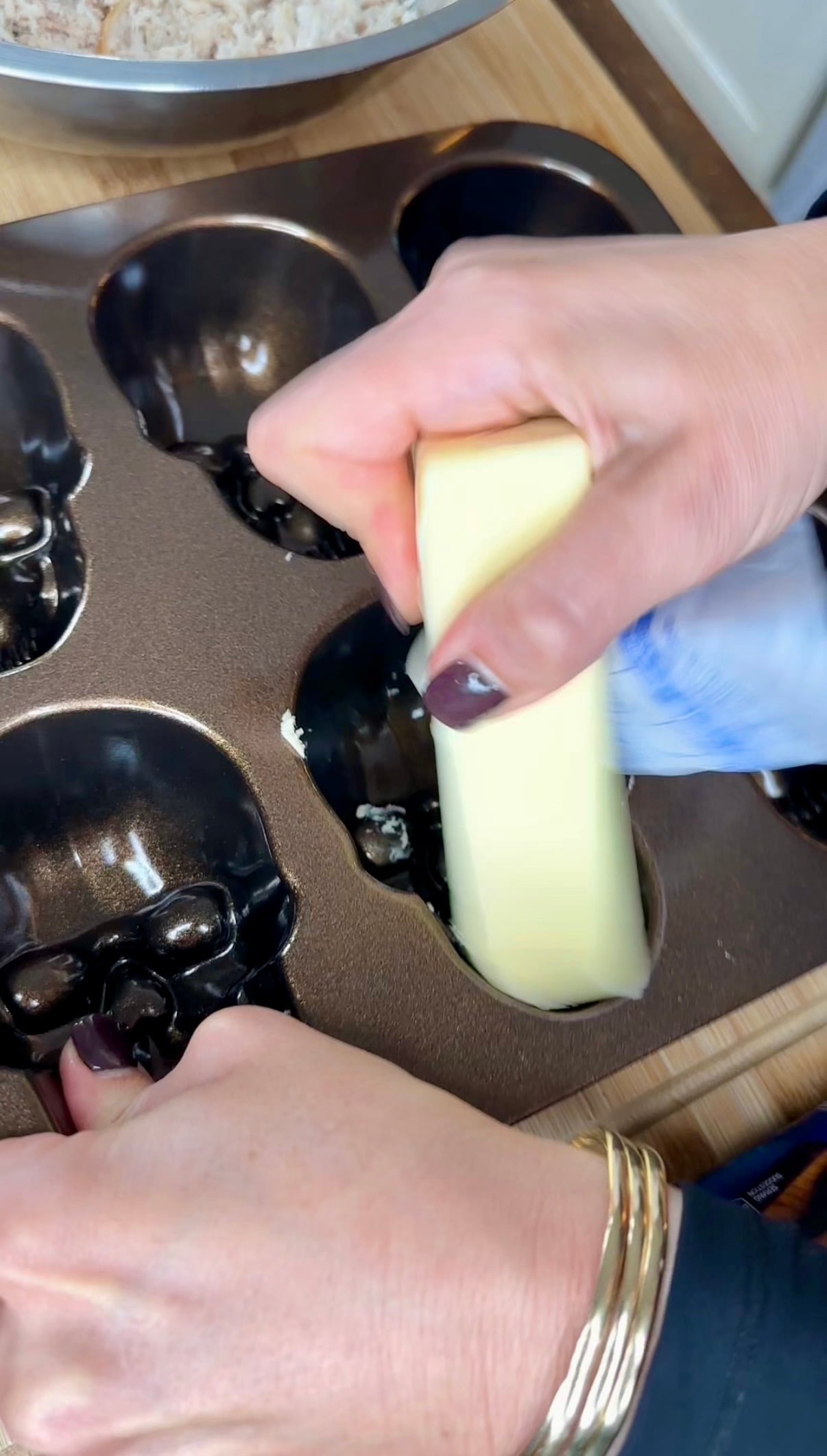Hands greasing a skull-shaped muffin tin with a stick of butter.