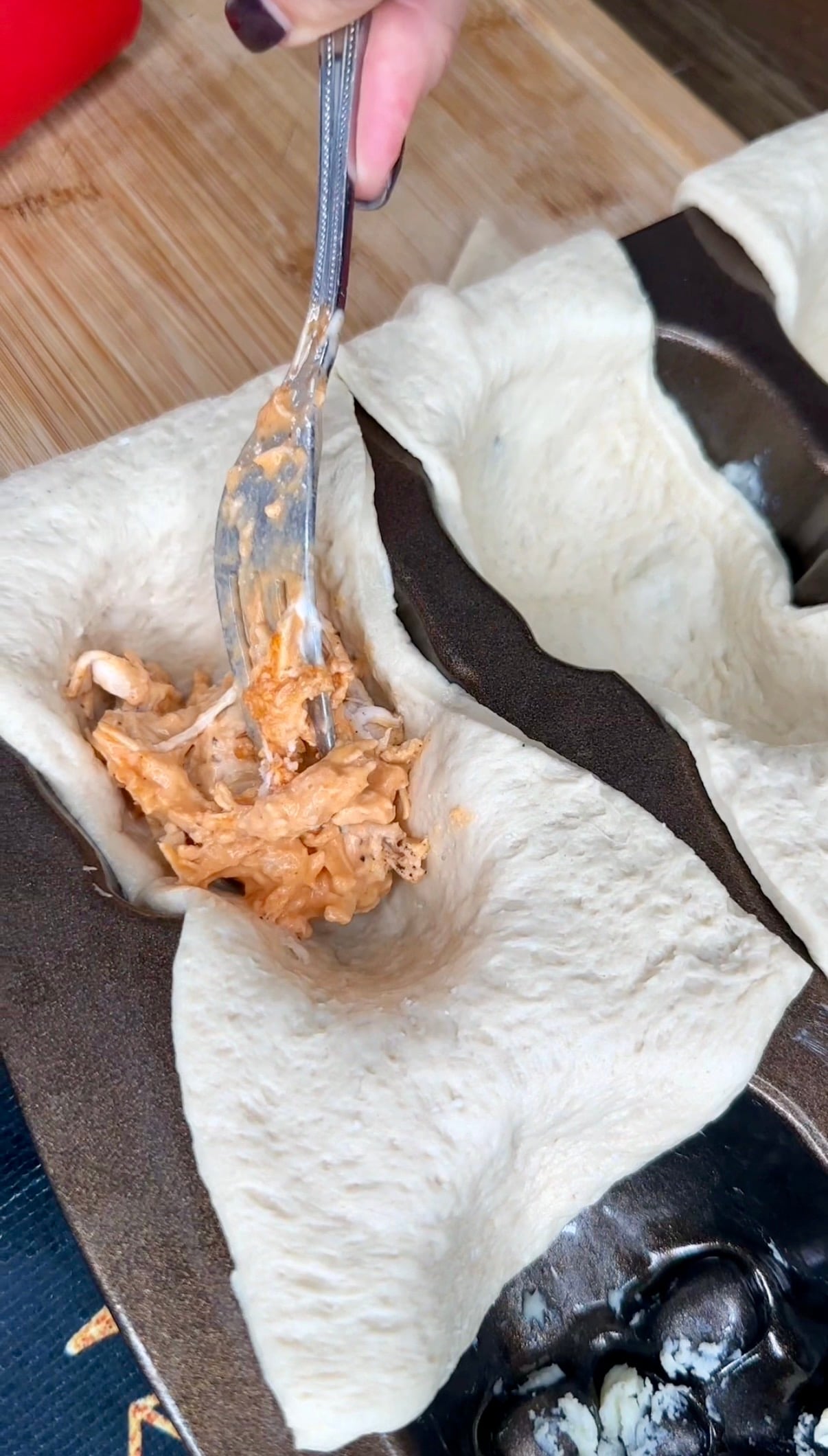 A hand uses a fork to fill a raw dough cup in a muffin tin with a creamy, shredded chicken mixture.