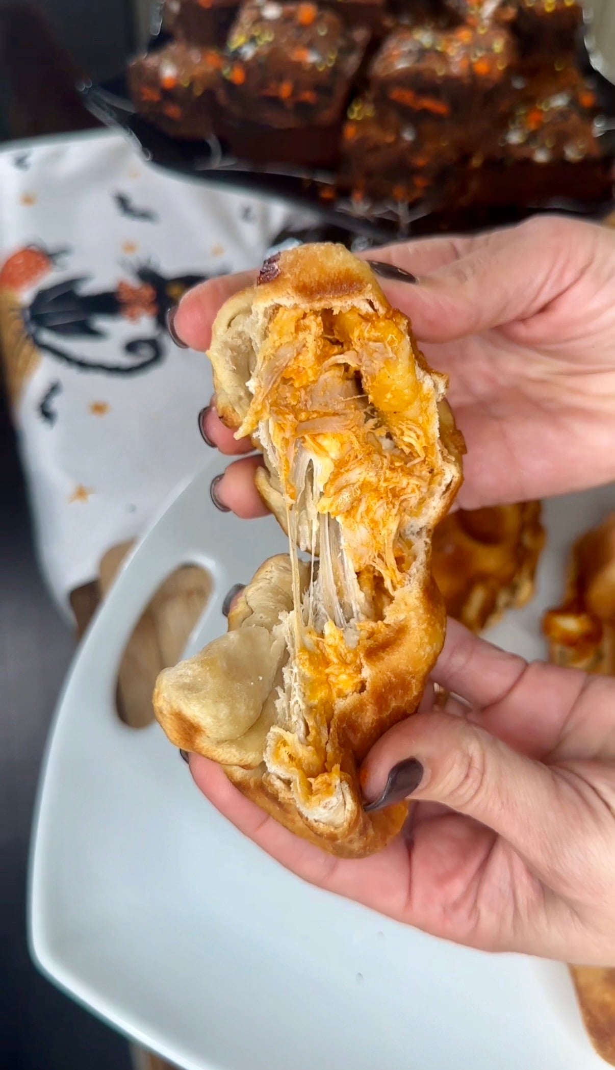 Hands pulling apart a golden-brown pastry filled with shredded meat and melted cheese, with a string of cheese stretching between the two halves.