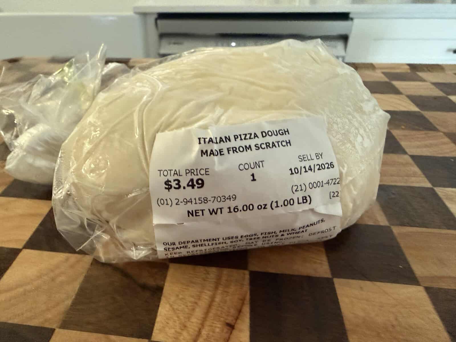 A ball of Grandma Jo’s Old-Fashioned Italian Spinach Pizza dough in plastic packaging with a label showing the price of $3.49 and a sell-by date of 10/14/2026.