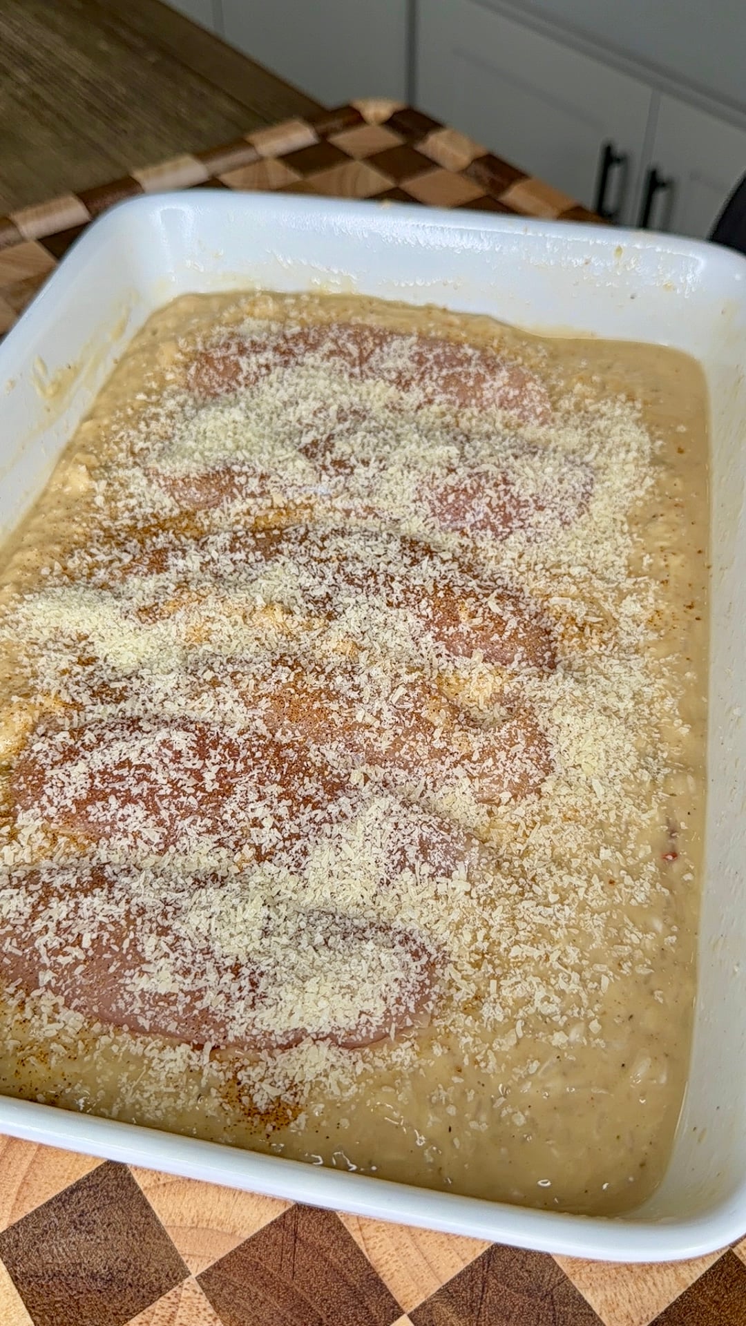 Raw chicken breasts topped with breadcrumbs in a baking dish filled with a creamy sauce.