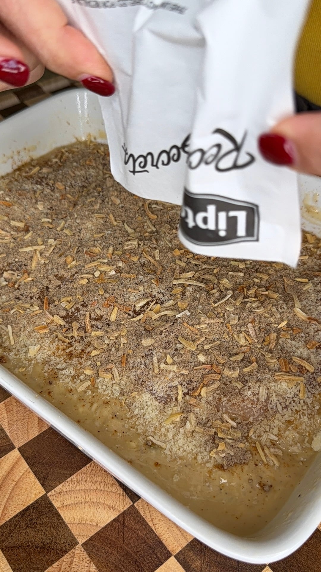 Hands pouring a packet of Lipton Recipe Secrets onion soup mix over a dish of meat.