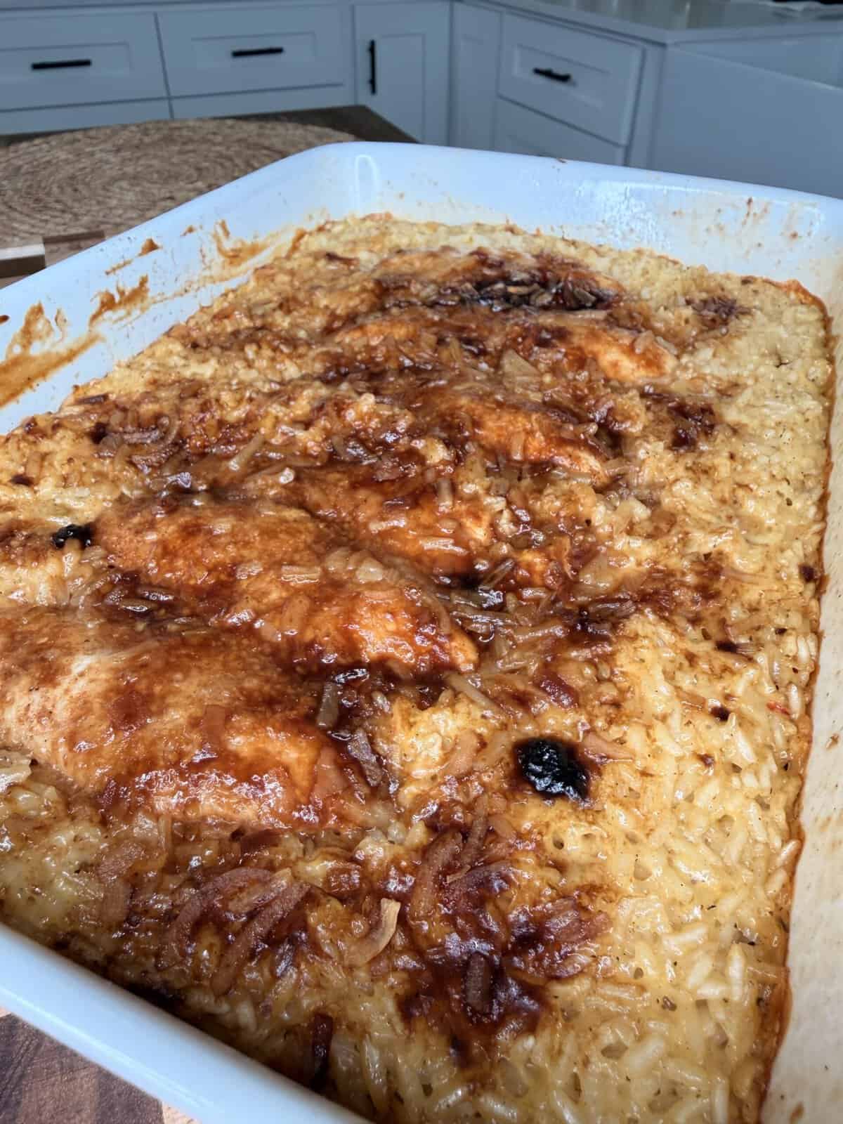 Baked chicken and rice casserole with a dark, caramelized glaze in a white baking dish.
