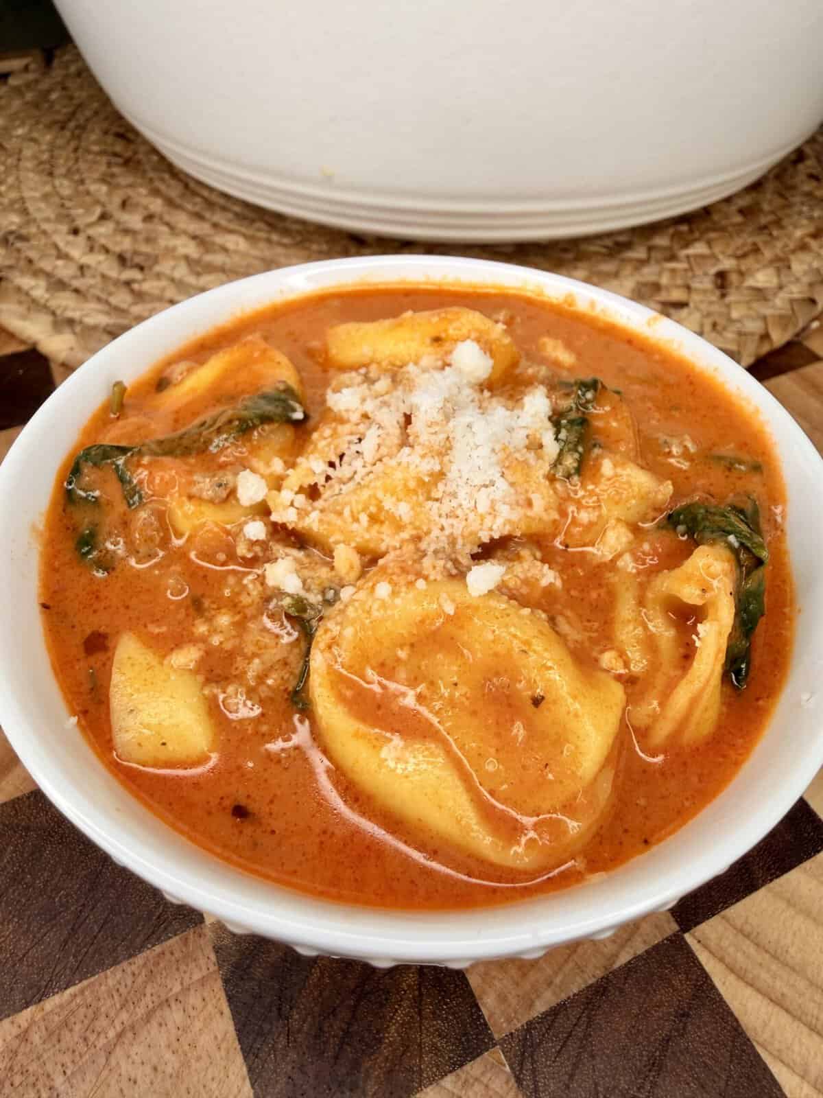 A bowl of creamy tomato soup with tortellini, spinach, and a dusting of grated cheese.