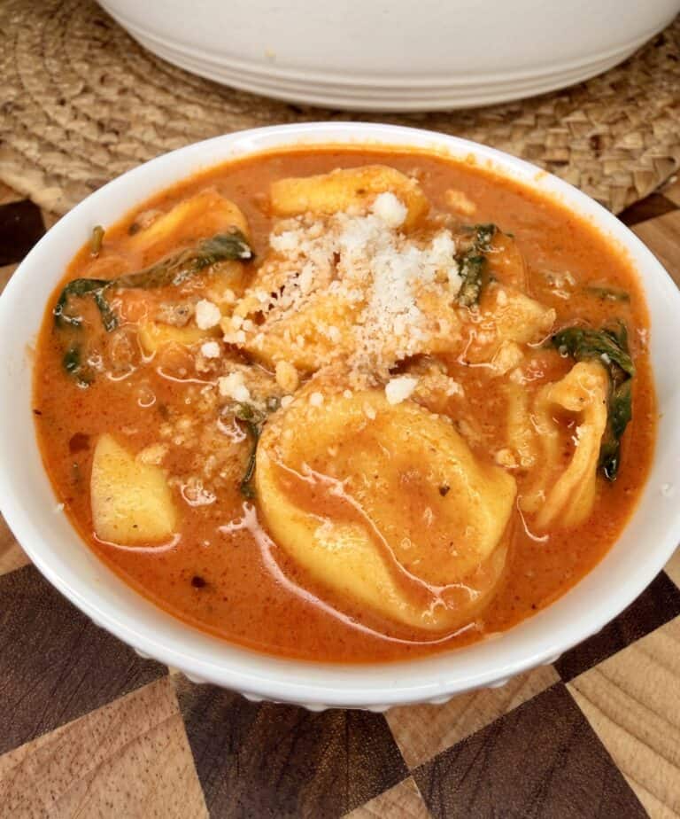 A bowl of tortellini soup with spinach and grated cheese.